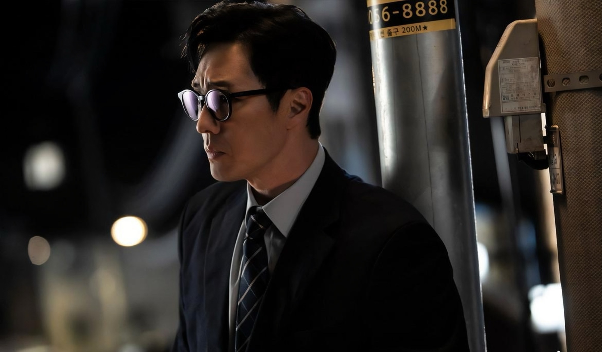 So Ji-sub as Manager Kim in a dark suit and glasses on a nighttime city street in Agent Kim Reactivated.