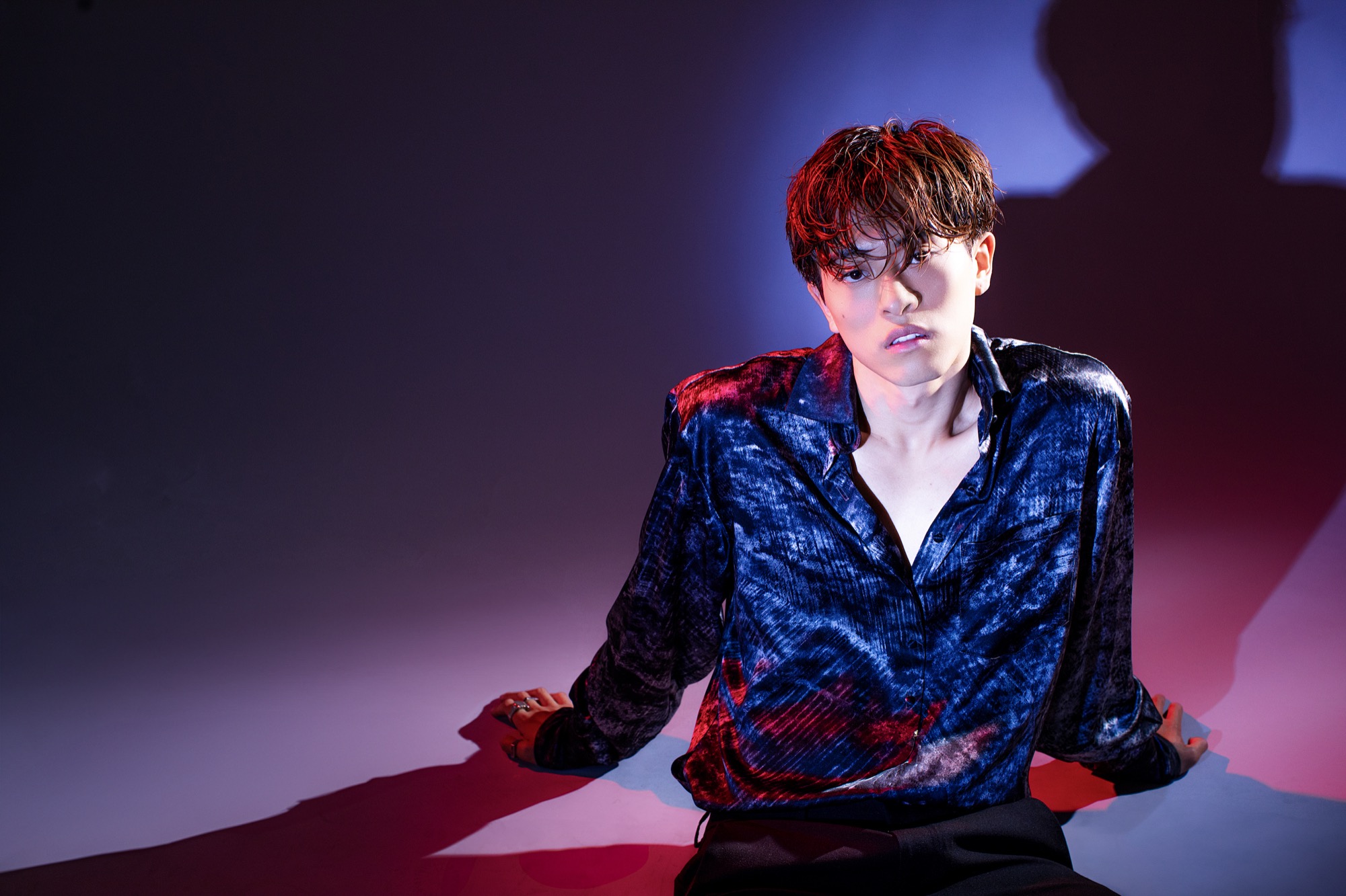 Alan Chikin Chow in a studio portrait, seated against a dark backdrop under blue and magenta light, looking toward camera.