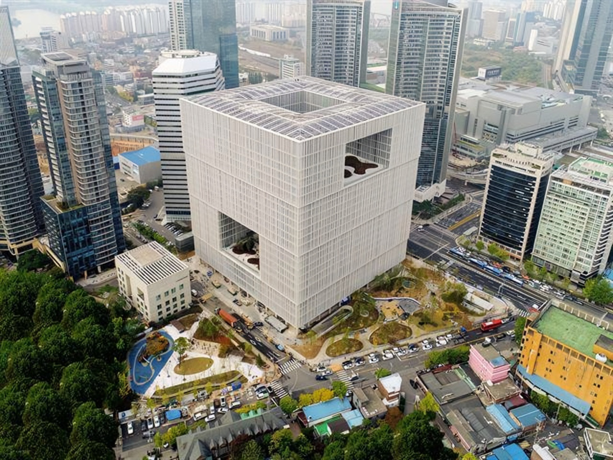 Aerial view of Amorepacific's modernist headquarters cube in Seoul's Yongsan District, with a landscaped courtyard and surrounding city towers.