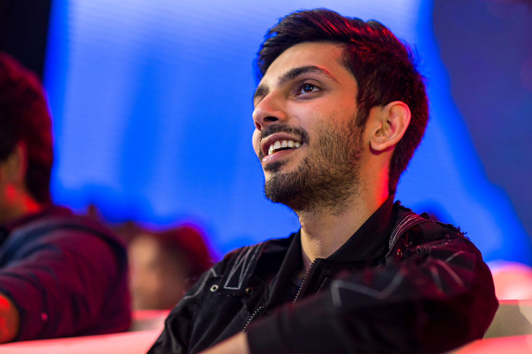 Anirudh Ravichander smiling in a black jacket, red light across his face, at an indoor launch.
