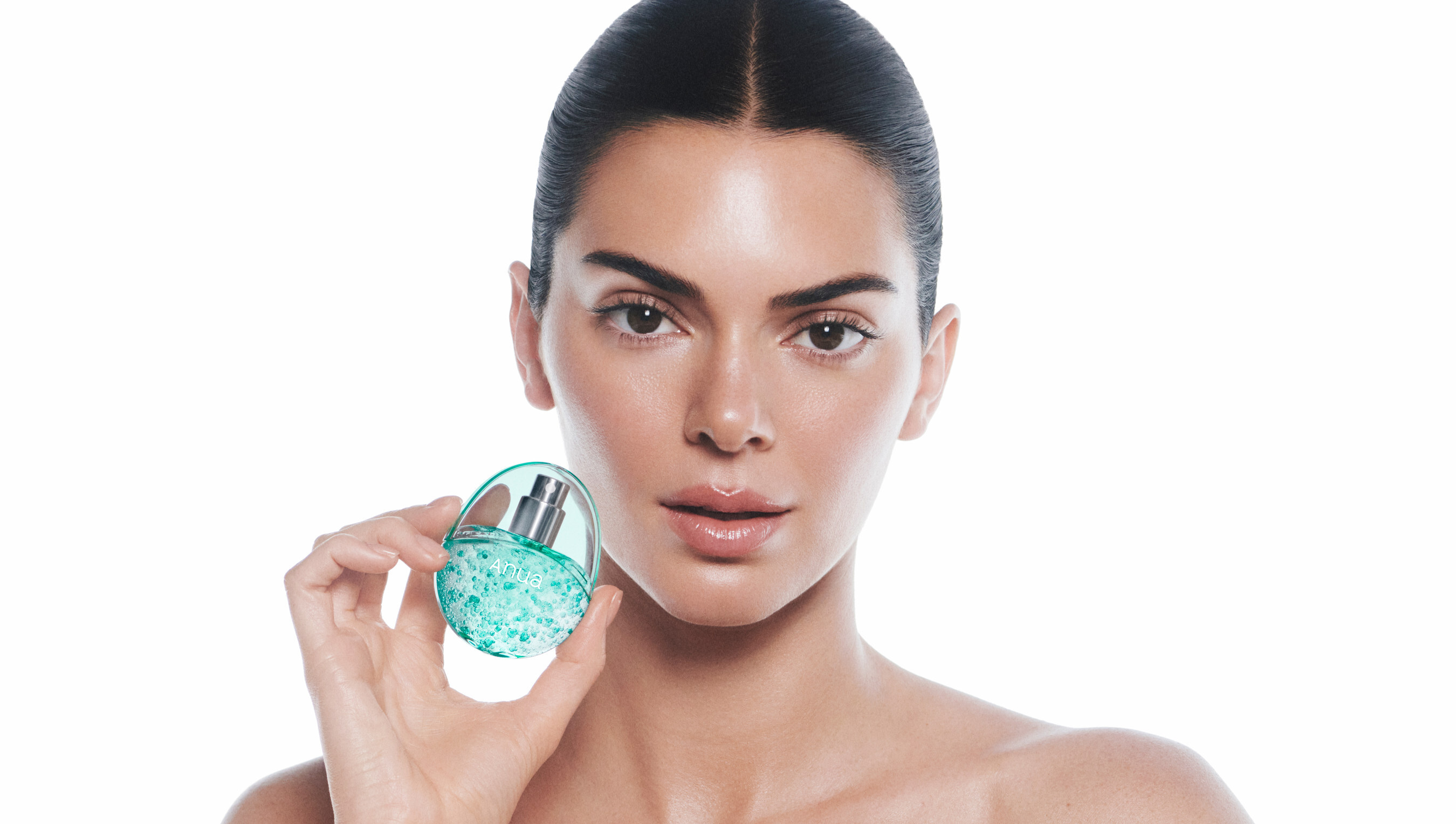 Kendall Jenner holding an Anua teal skincare bottle against a bright white studio background for the brand's global ambassador campaign.