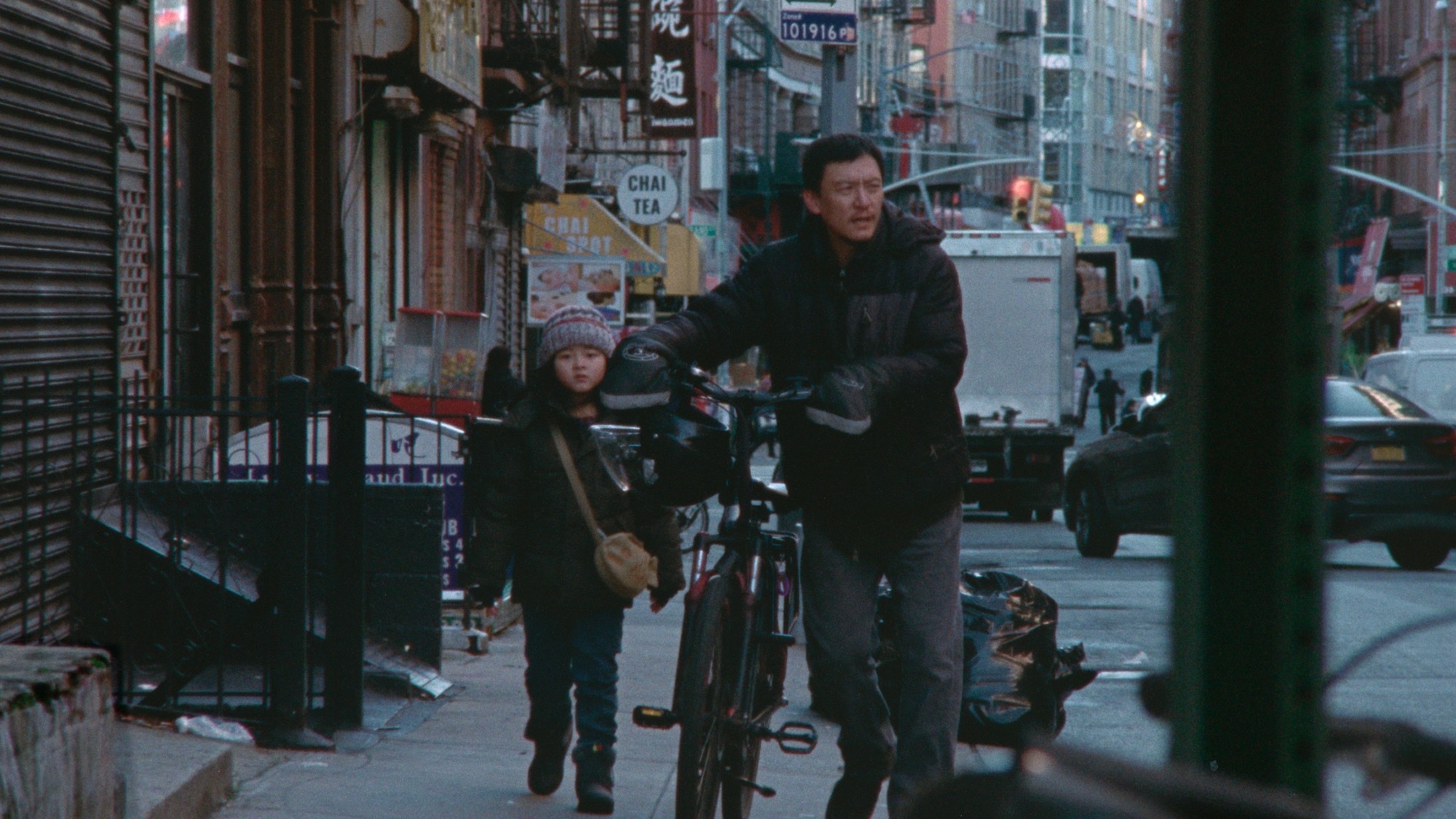 Chang Chen as delivery driver Lu walks a bicycle beside a young girl on a New York Chinatown sidewalk in Lloyd Lee Choi’s Lucky Lu.