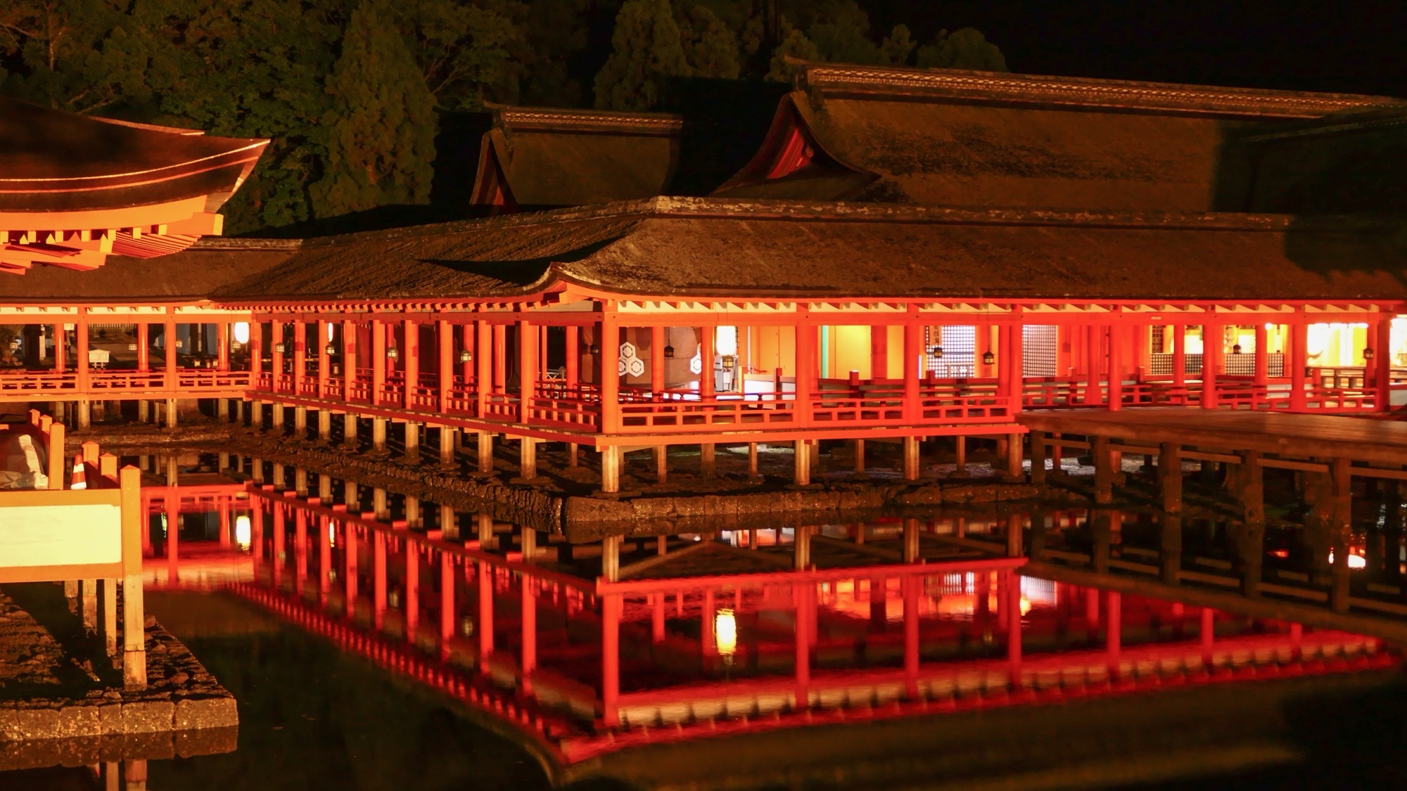 Empty vermilion corridors of Itsukushima Shrine at night, reflected in still water.