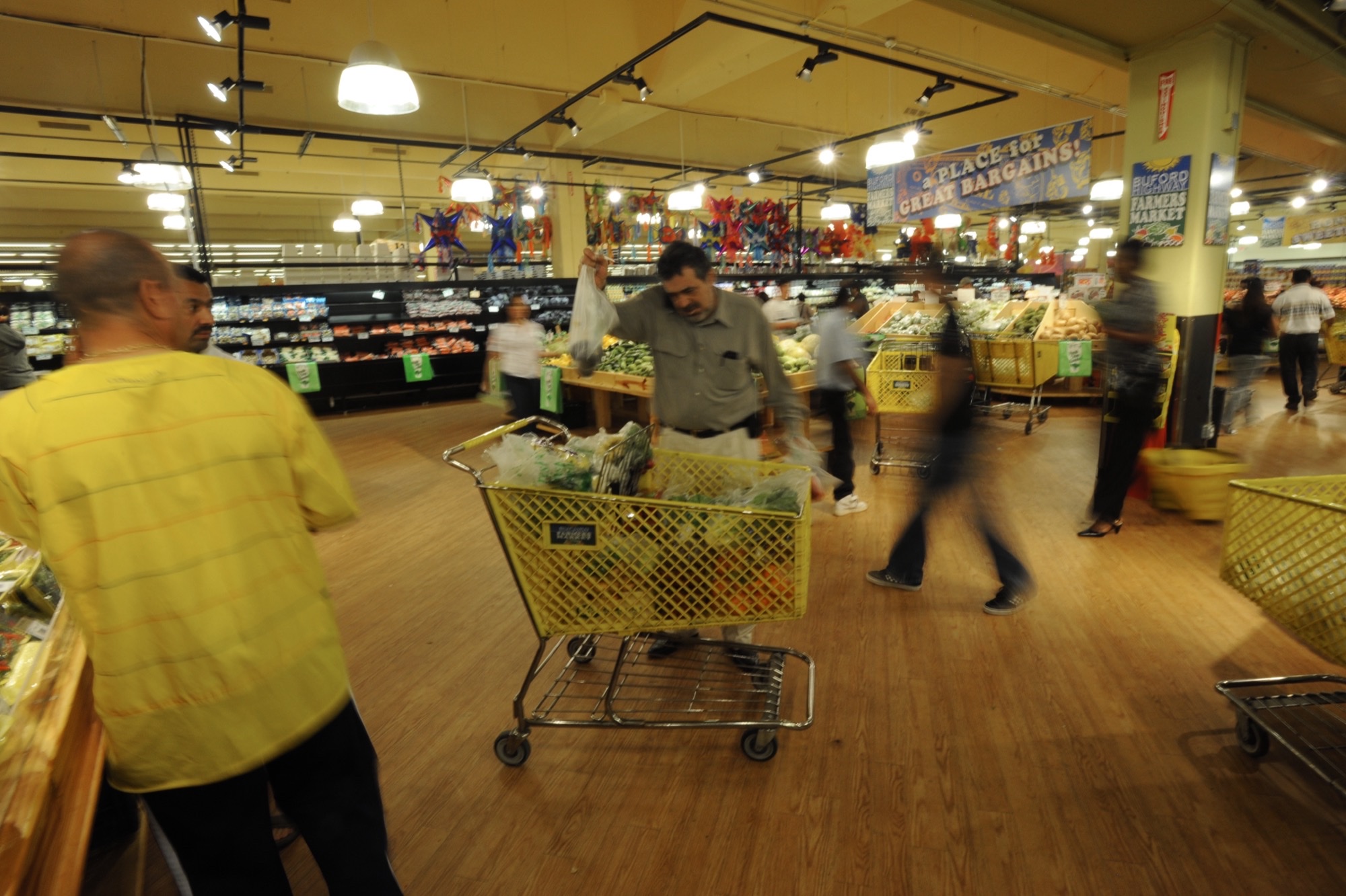 Shoppers with yellow carts inside Buford Highway Farmers Market in Doraville, under a Buford Highway Farmers Market banner.
