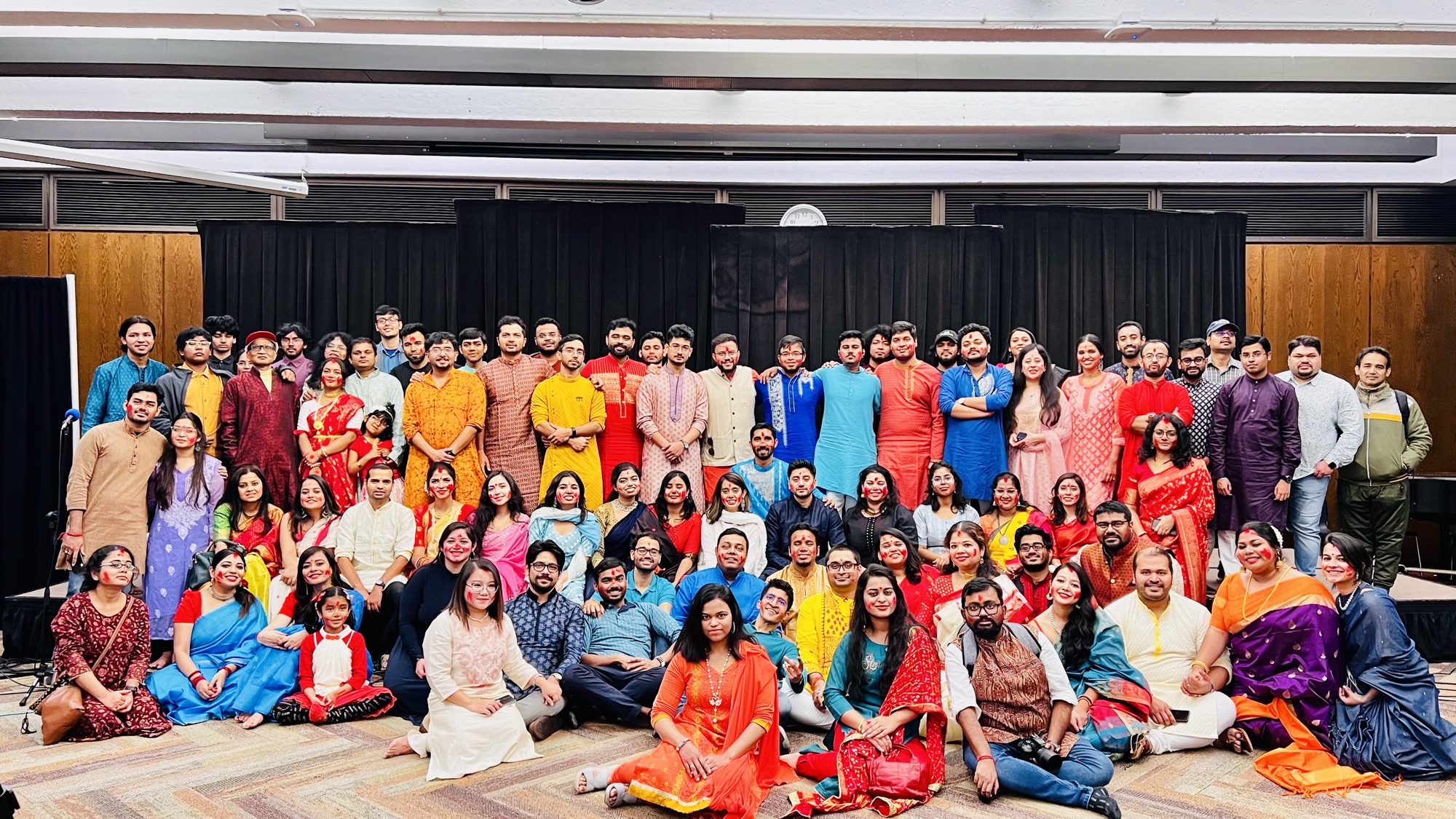 Large Bengalis In Chicago community group in festive wear posed indoors at a prior hall celebration.