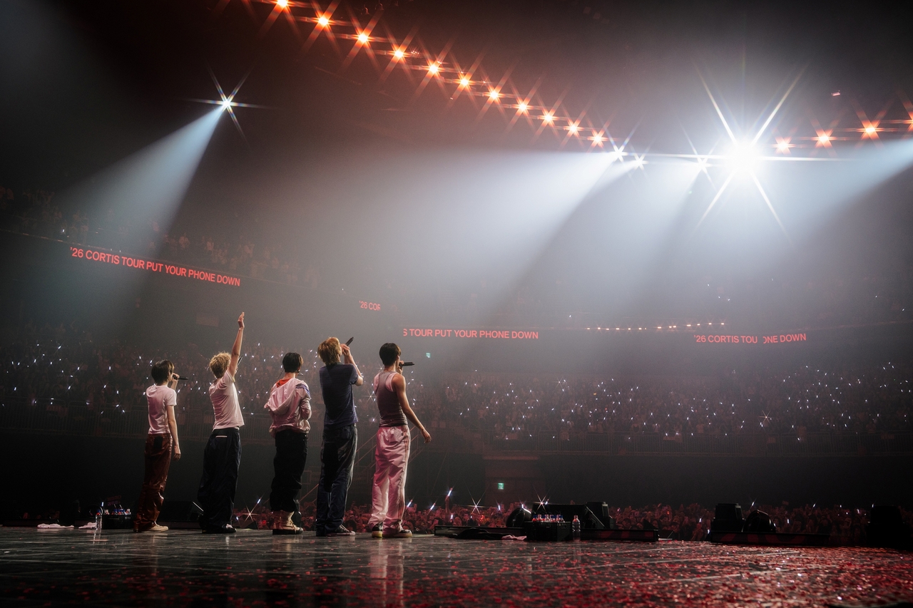 Cortis onstage during the Put Your Phone Down tour, facing a packed arena with tour banners overhead.