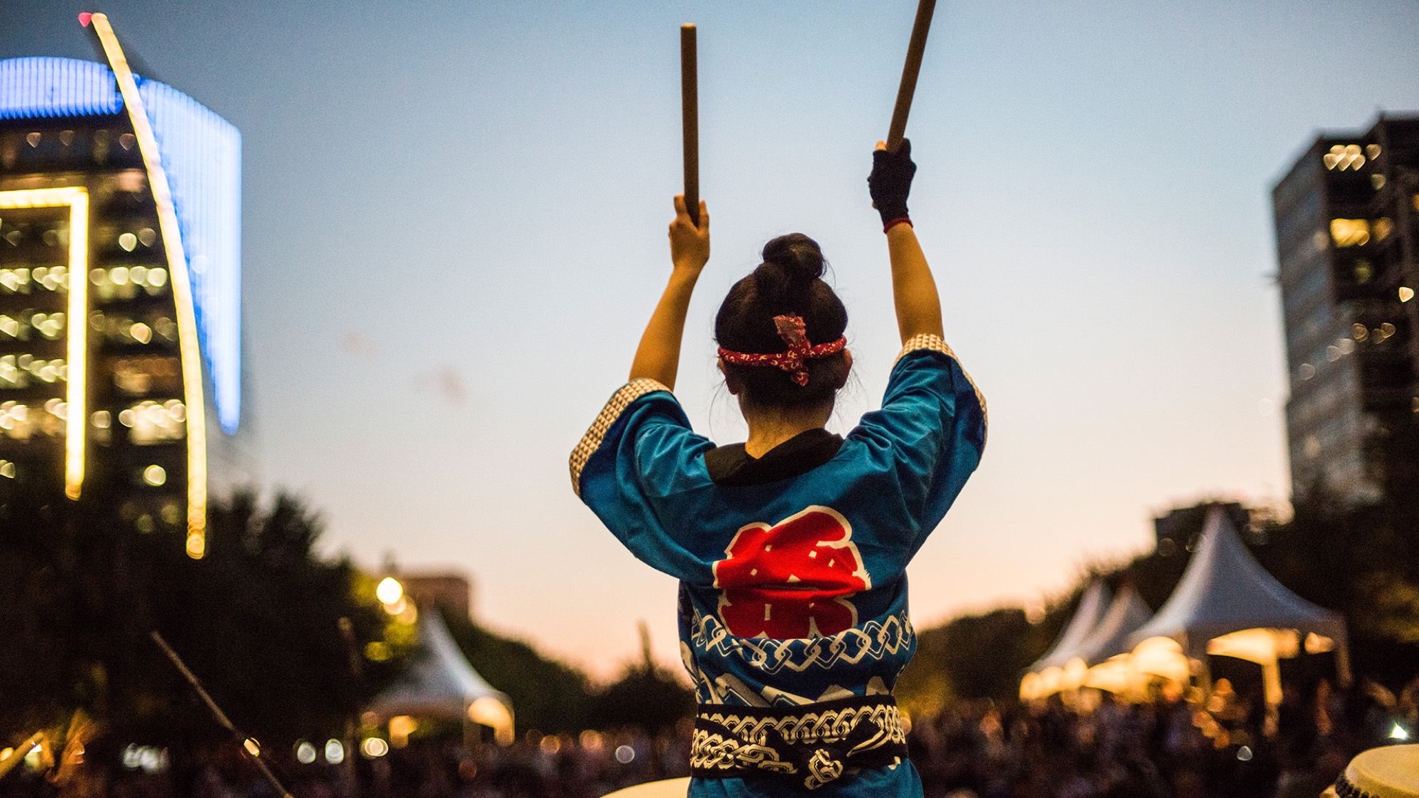 A taiko performer raises drumsticks at dusk during a Crow Museum outdoor program.