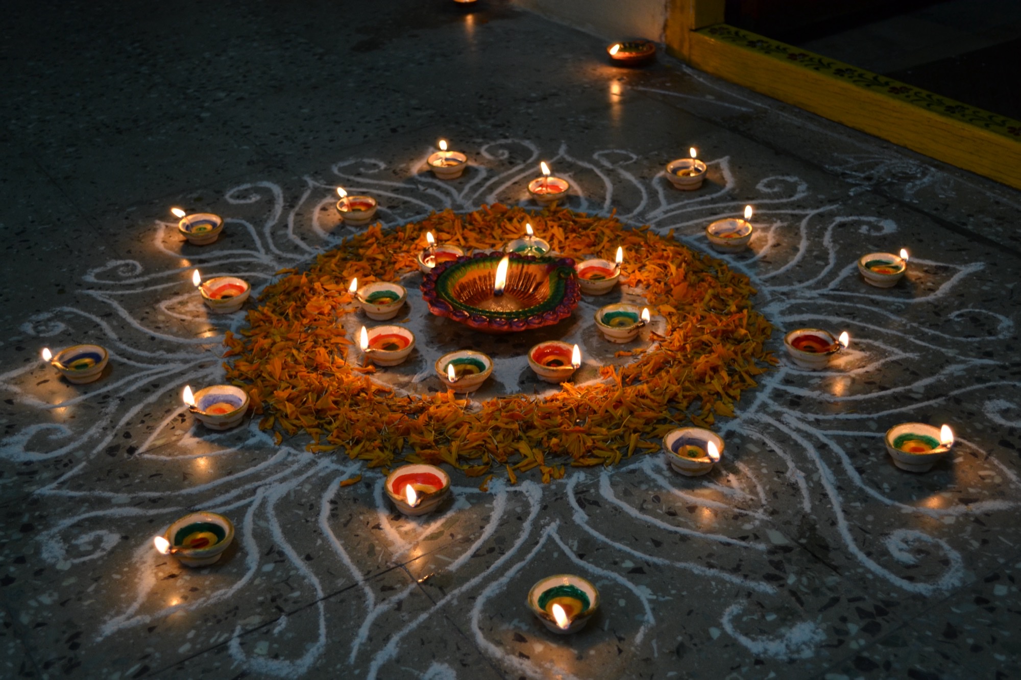Lit clay diyas set in a white rangoli ring with marigold petals on a stone floor.