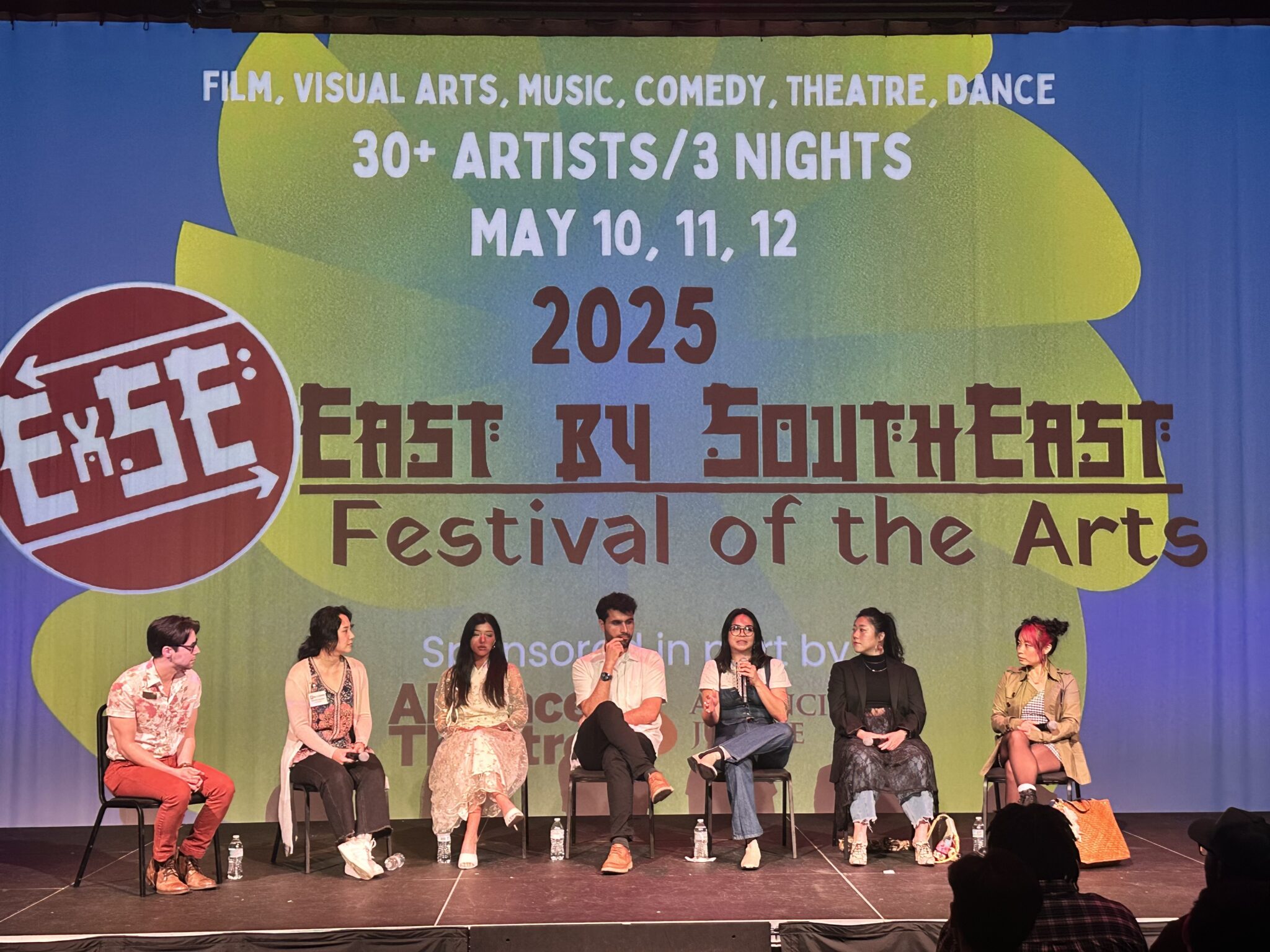 Seven panelists sit onstage under a 2025 East by Southeast Festival of the Arts banner during a prior edition, May 10 through 12.