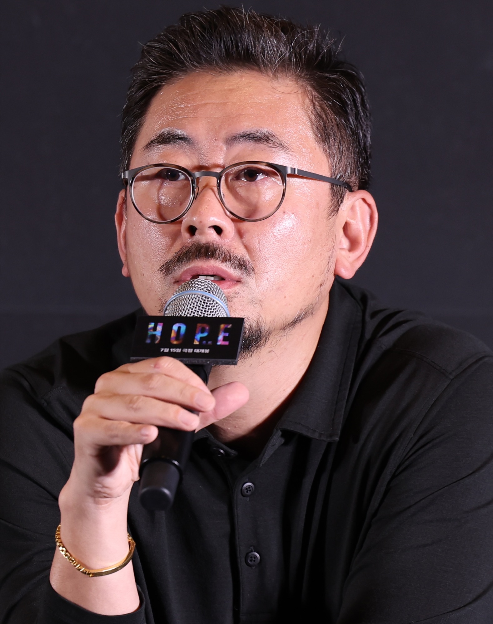 Director Na Hong-jin speaks into a Hope-branded microphone at a 2026 press event for the film.