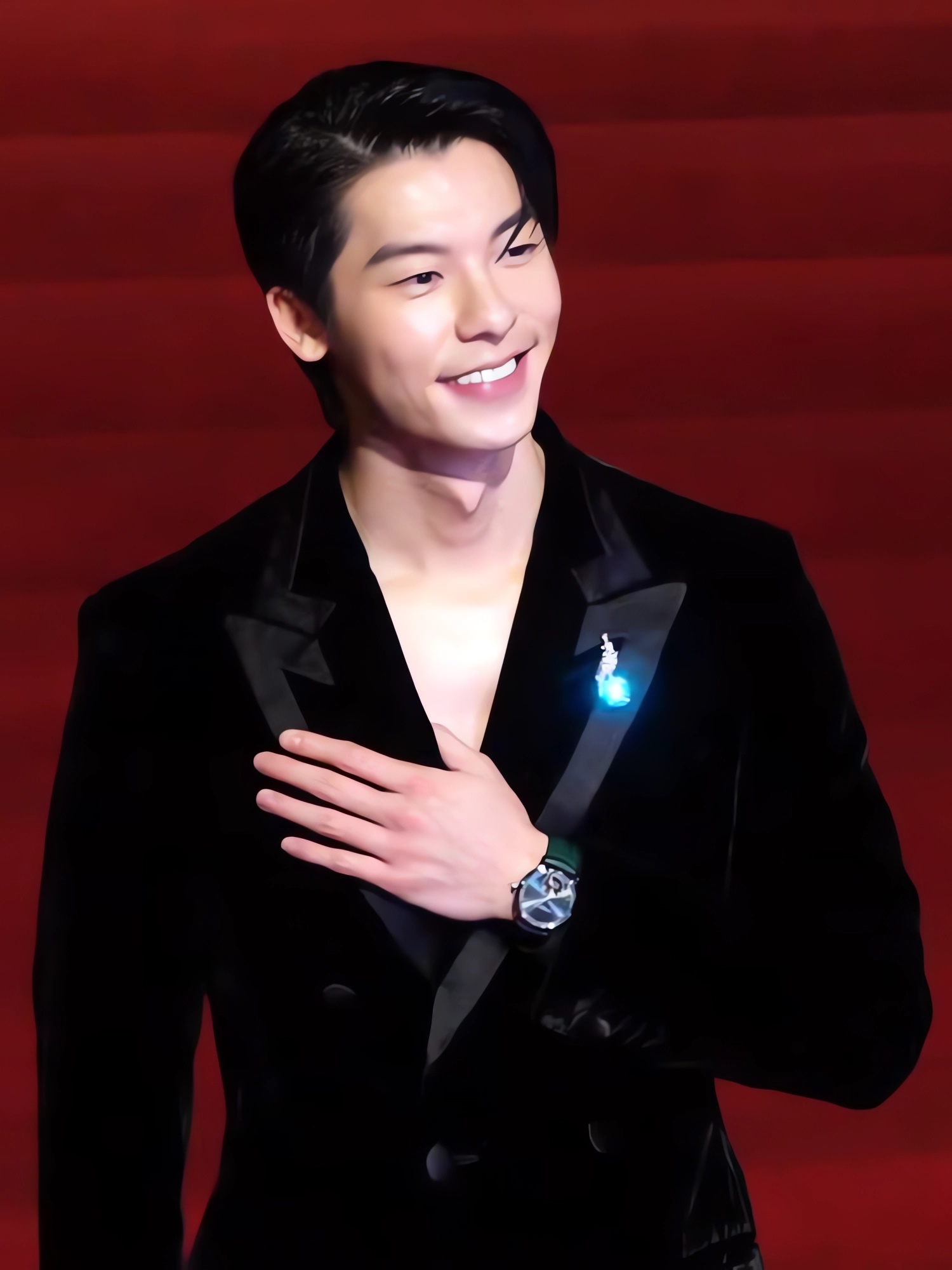 Hsu Kuang-han in a black velvet tuxedo on the Golden Horse Awards red carpet, hand on his chest, smiling against a red backdrop.