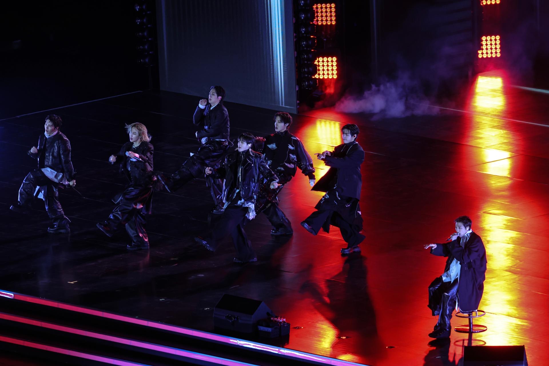 BTS perform in black stage looks on a dark floor under red and gold lights during the ARIRANG comeback concert at Gwanghwamun Square in Seoul.
