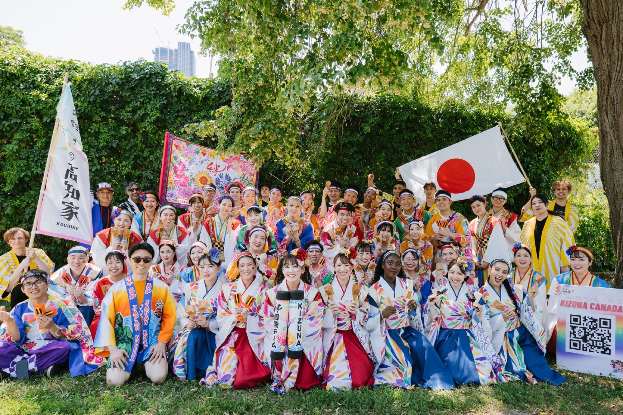 Yosakoi dancers in happi coats pose outdoors with naruko clappers and a Japanese flag at a Canada Japan festival gathering.