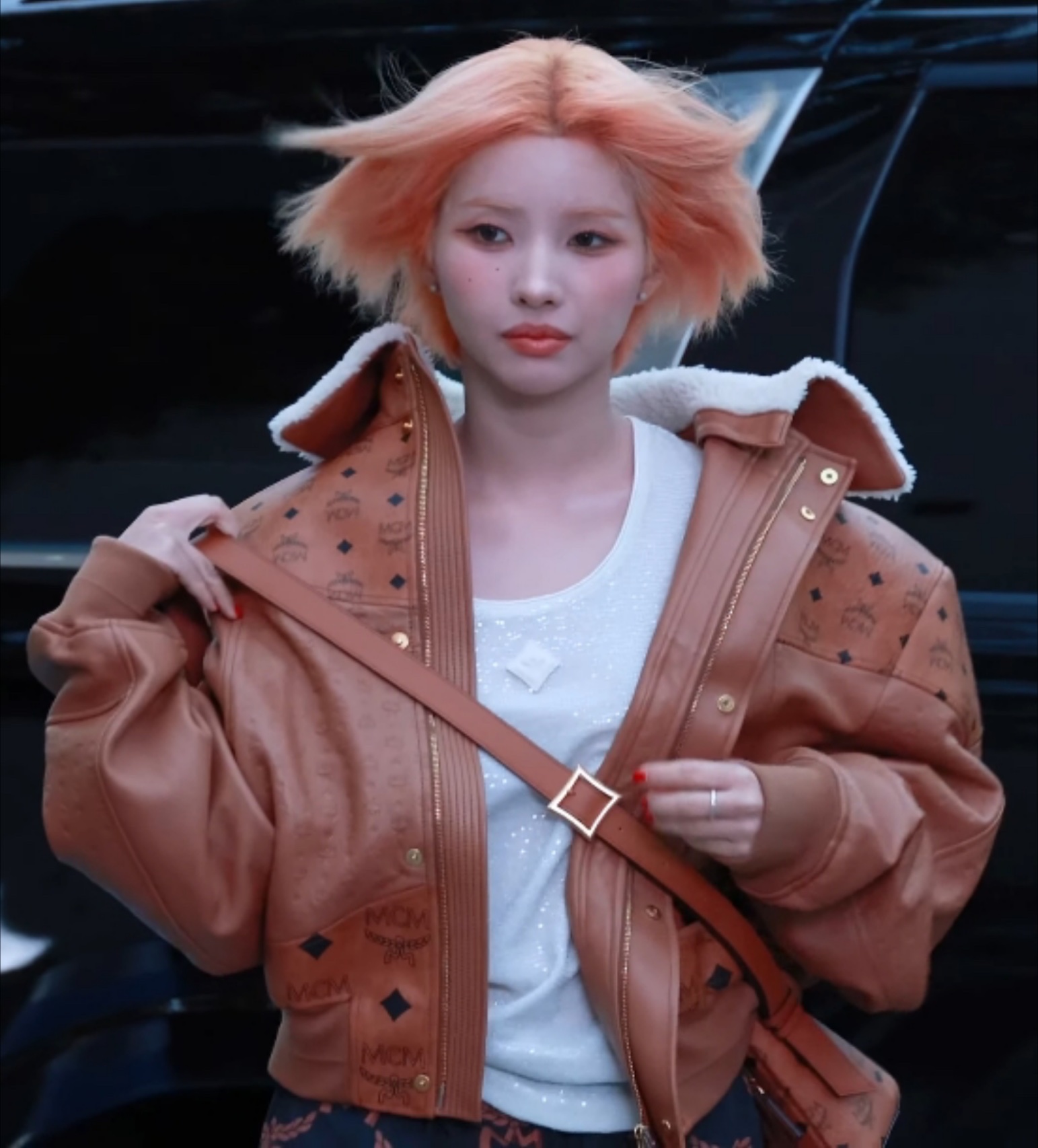 Jeon So-yeon with short peach hair in a brown MCM jacket with a shearling collar, holding a bag strap at a 2024 fashion photocall.