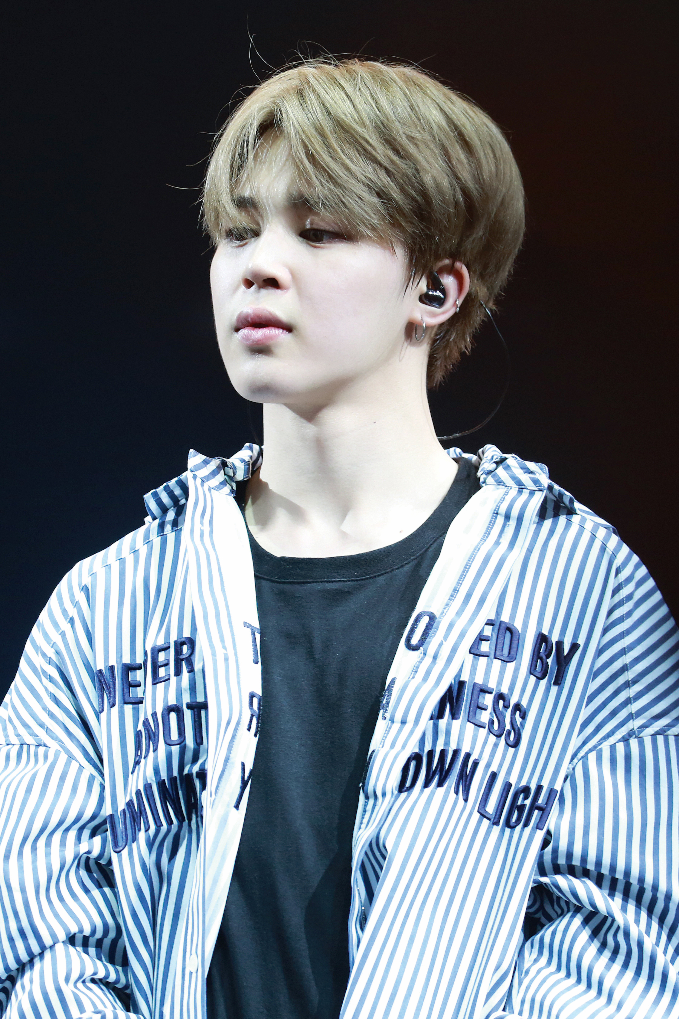 Jimin of BTS on stage in a close-up during The Wings Tour stop in Anaheim, wearing an in-ear monitor.