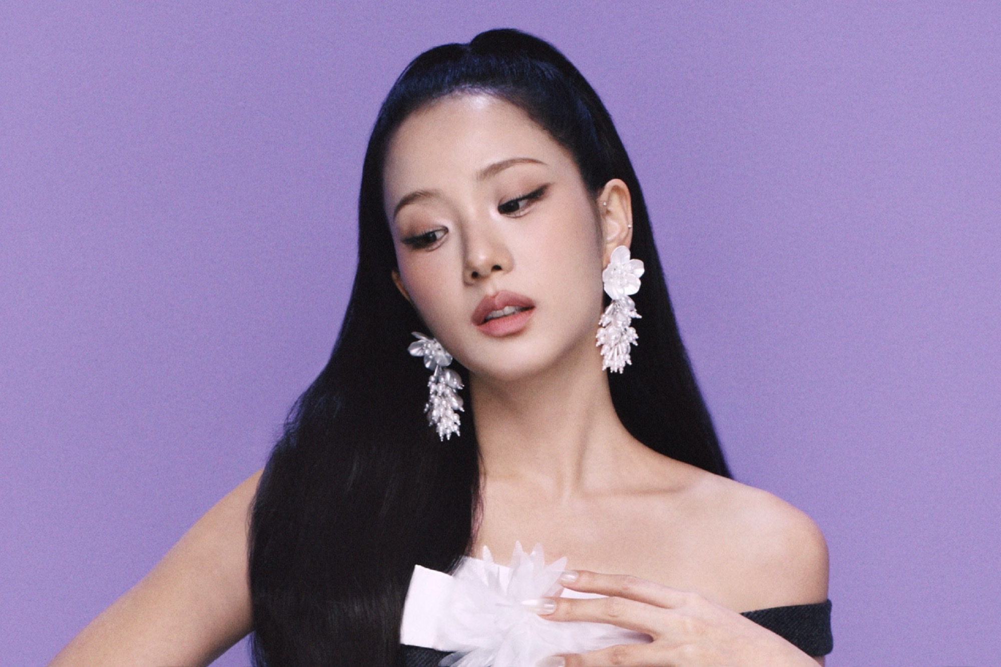 Jisoo with long black hair and crystal earrings against a purple backdrop, one hand at her collarbone.