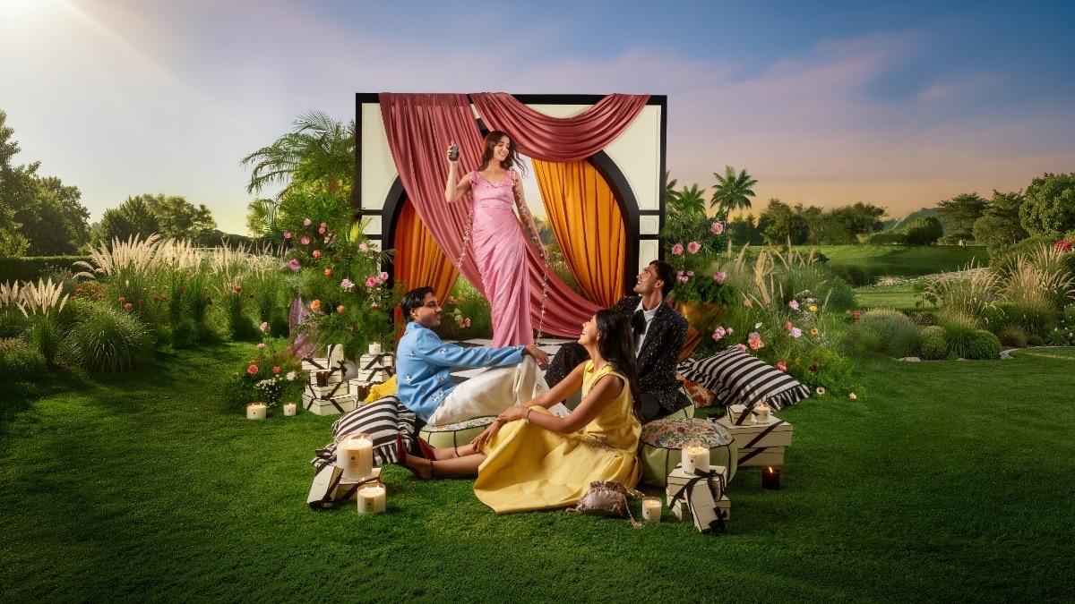 Four people in a Jo Malone London Diwali campaign garden scene with lit candles, cream gift boxes, and draped pink and saffron fabric behind them.