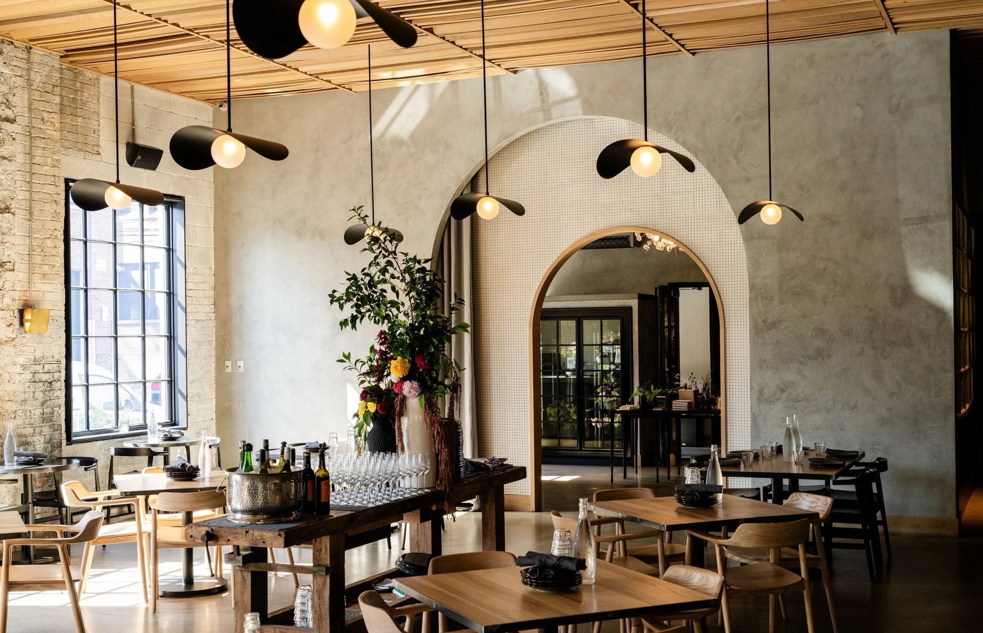Sunlit dining room at Maxwells Trading in Chicago’s Kinzie Industrial Corridor, with wood tables set for service under arched tile detailing.