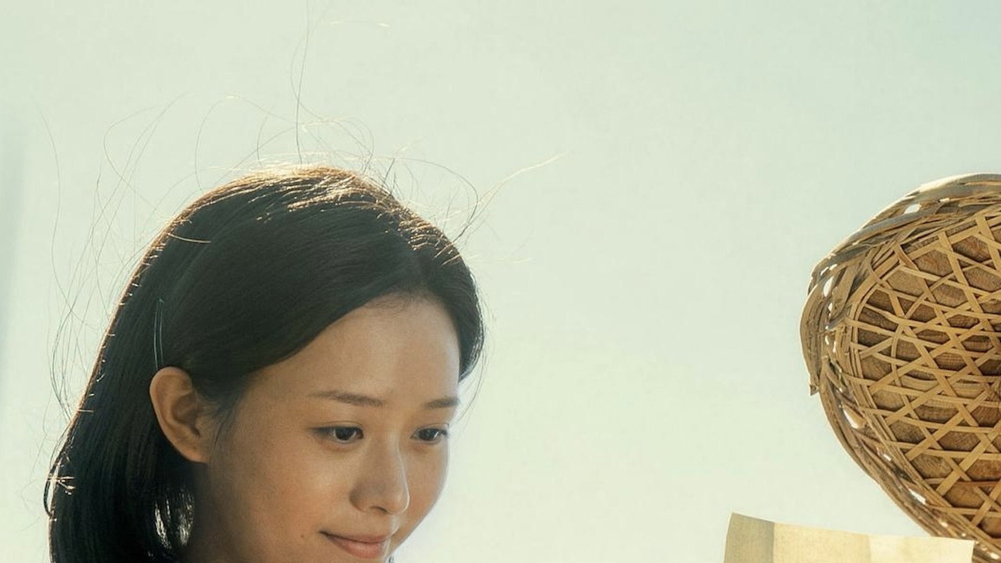 Li Sitong as Xie Nanzhi in Dear You, looking down at a letter in bright outdoor light, a woven hat just in frame.