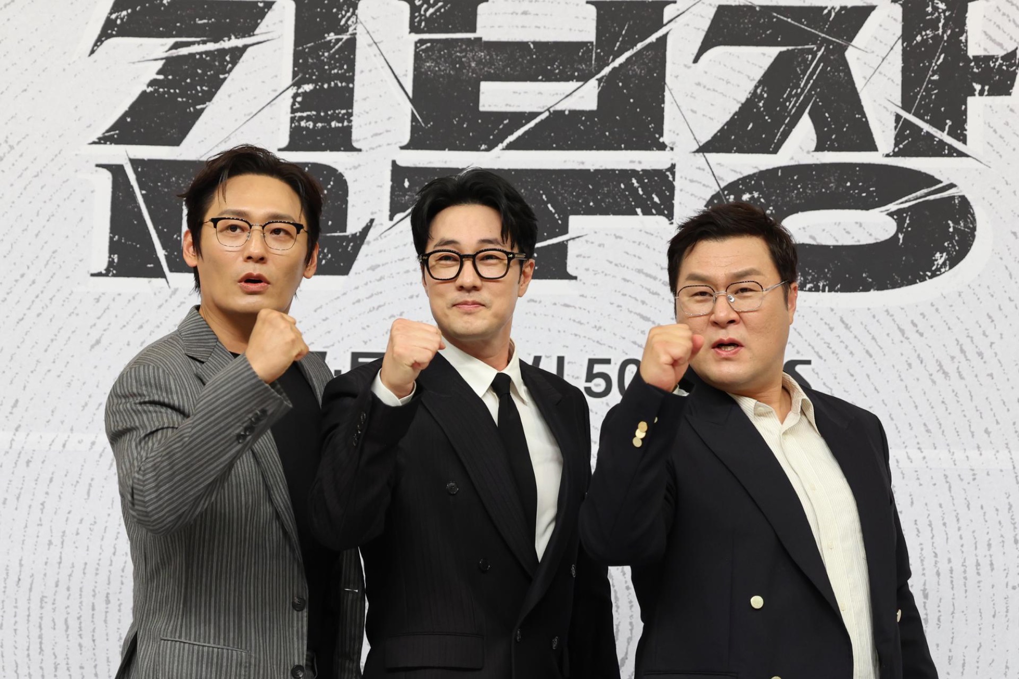 Choi Dae-hoon, So Ji-sub, and Yoon Kyung-ho at an Agent Kim Reactivated press event, fists raised against the show's promotional backdrop.
