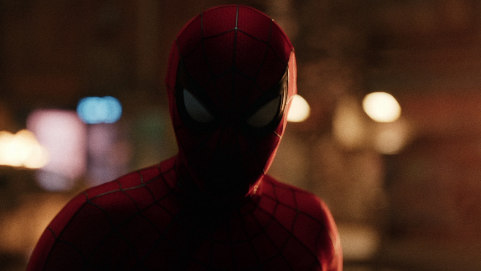 Close-up of Spider-Man in his red mask against blurred city lights at night.