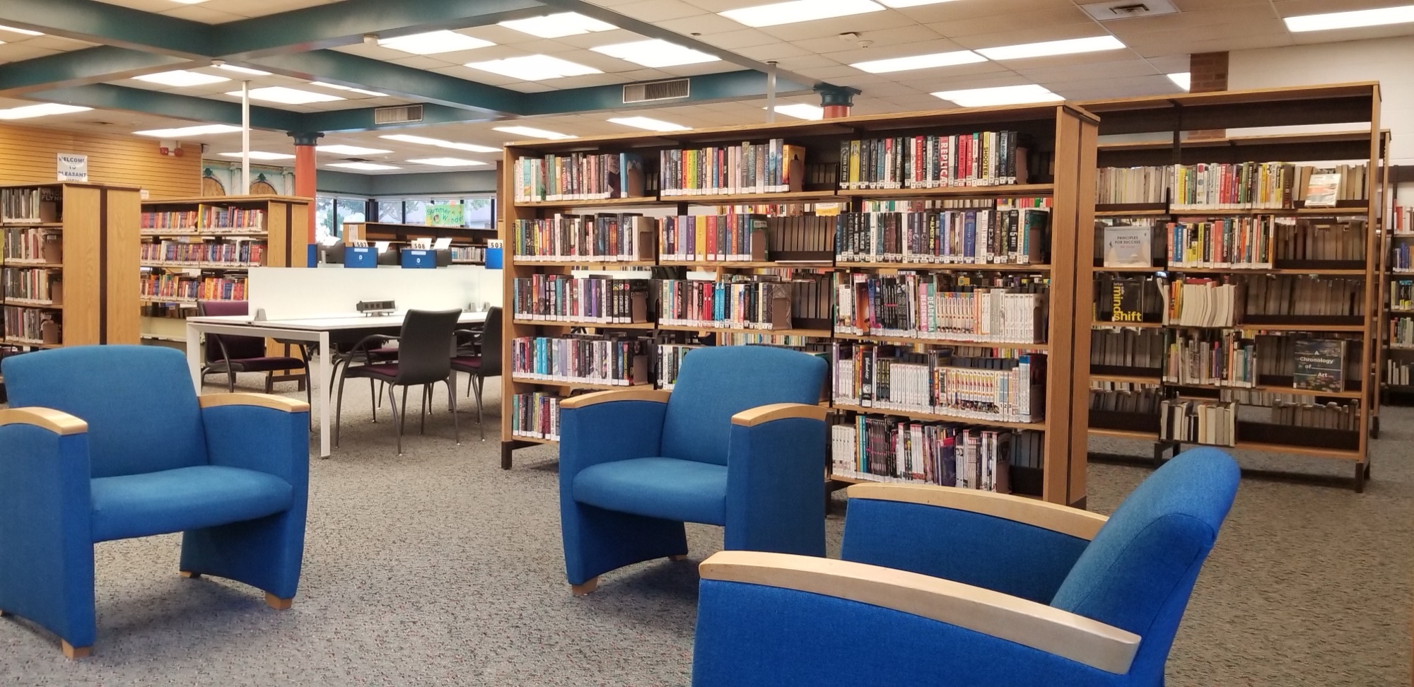 Open stacks and reading tables inside Pleasant View Toronto Public Library, with shelves of books lining a bright interior corridor.
