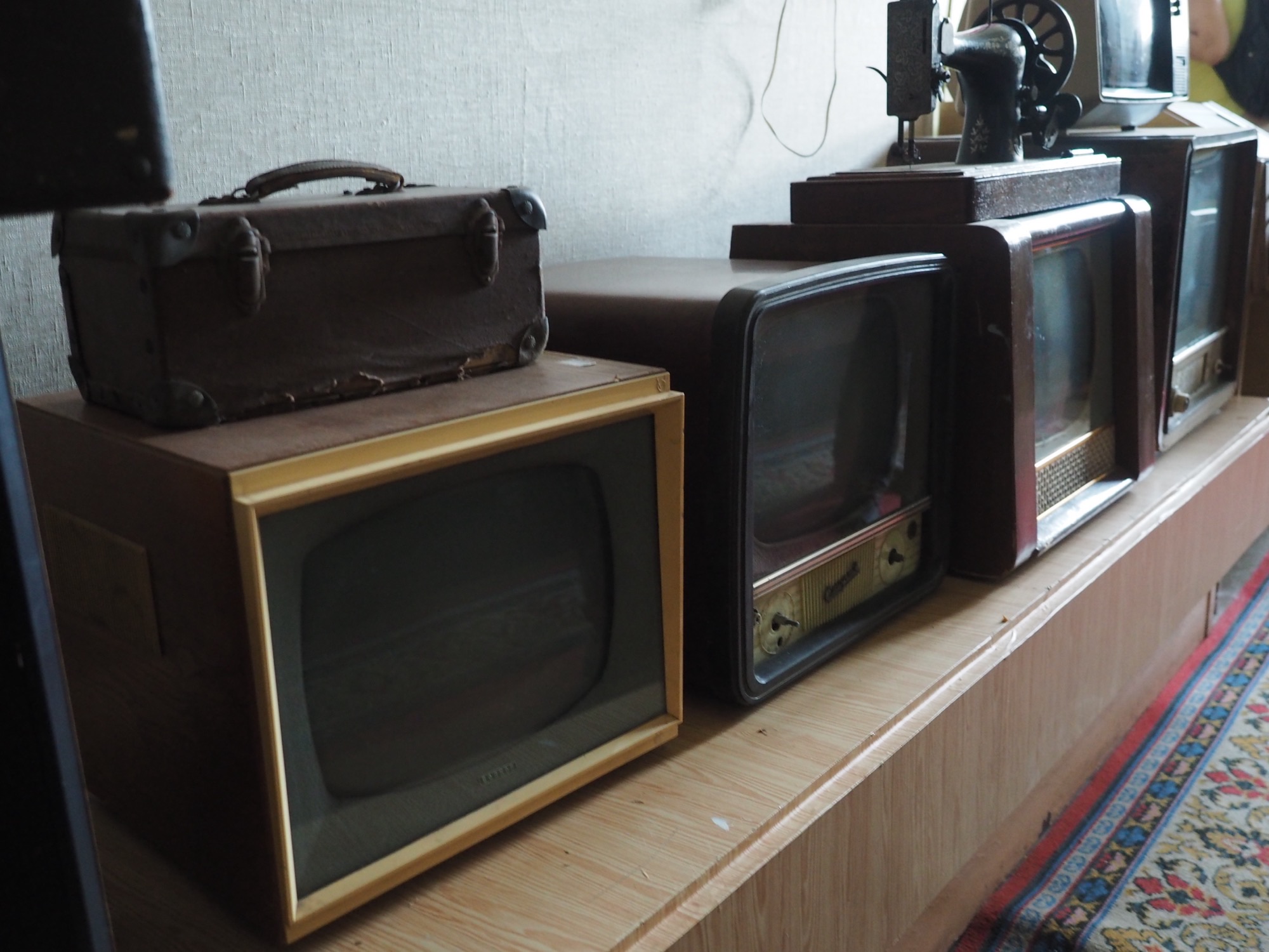 Four old CRT tube television sets stacked against a wall, a visual nod to cursed-media J-horror.