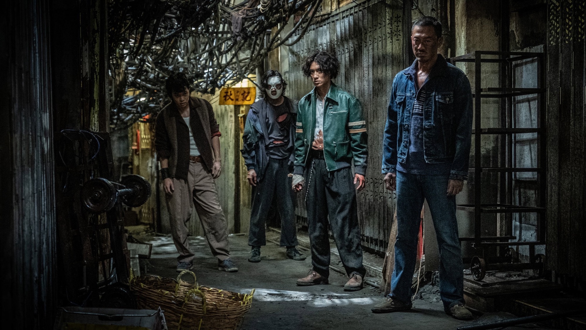 Raymond Lam in a green jacket and Louis Koo in denim stand with co-stars in a cramped Kowloon Walled City alley in Twilight of the Warriors: Walled In.