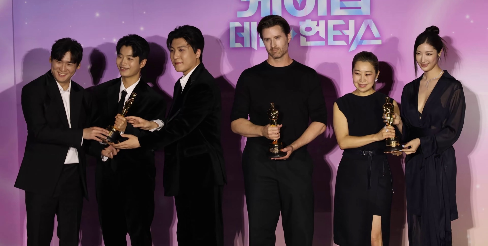 KPop Demon Hunters creative team at an Academy Award win press conference, holding Oscar statues.