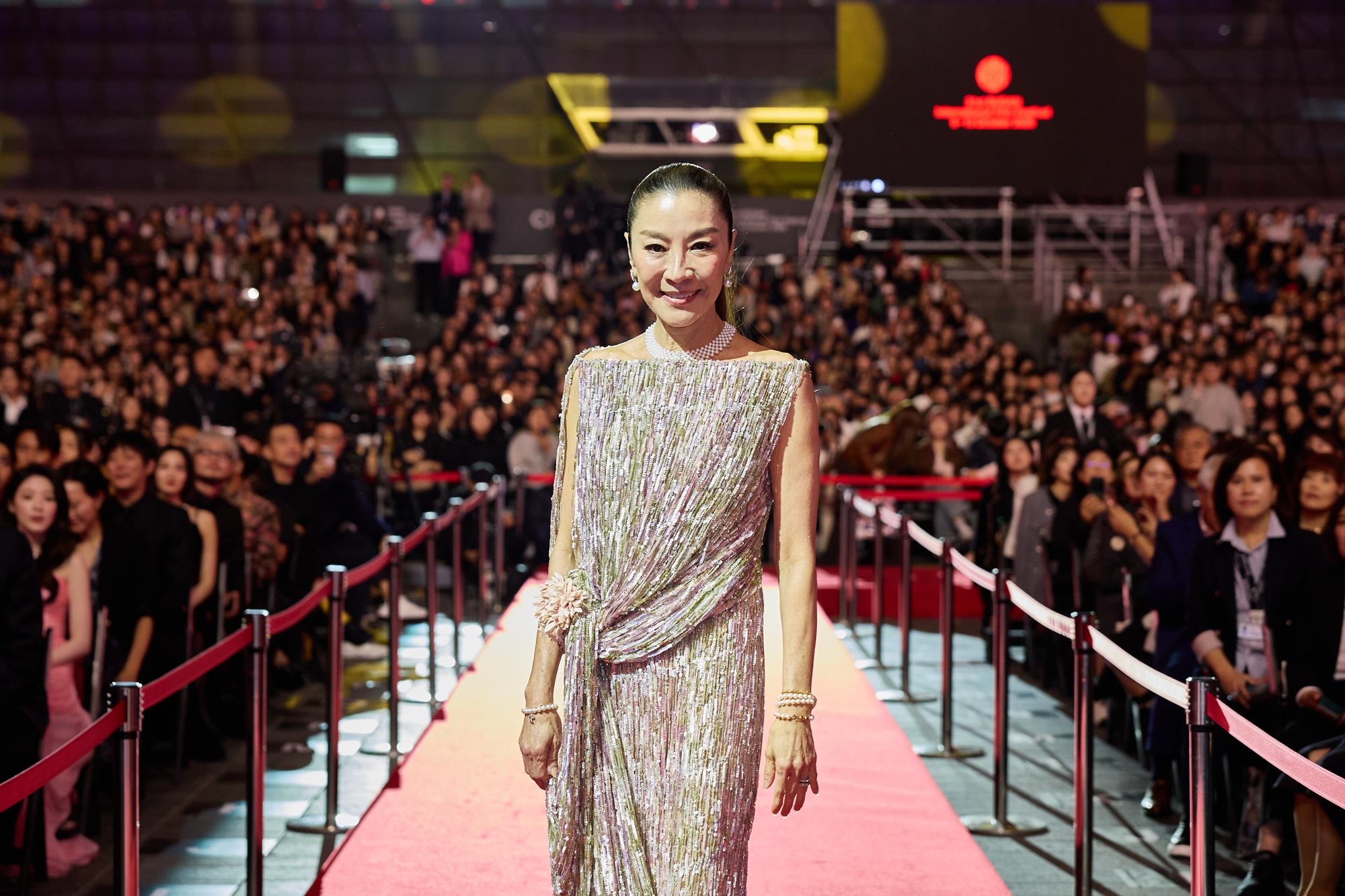Michelle Yeoh in a shimmering gown and pearls smiling on the red carpet at the Busan Cinema Center for the 31st BIFF opening.