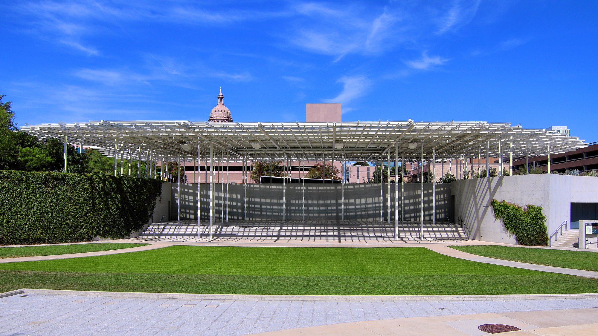 Moody Amphitheater’s lattice canopy and lawn at Waterloo Park in Austin, with the Texas State Capitol dome visible beyond the stage.