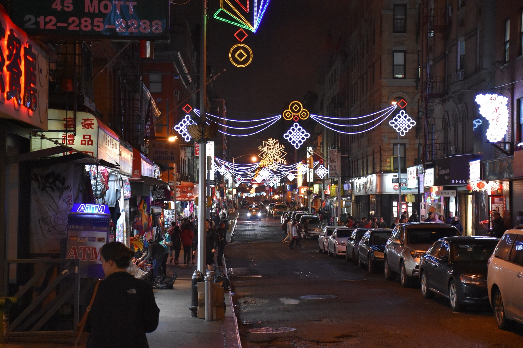 Mott Street in Manhattan Chinatown at night with festive overhead lights.