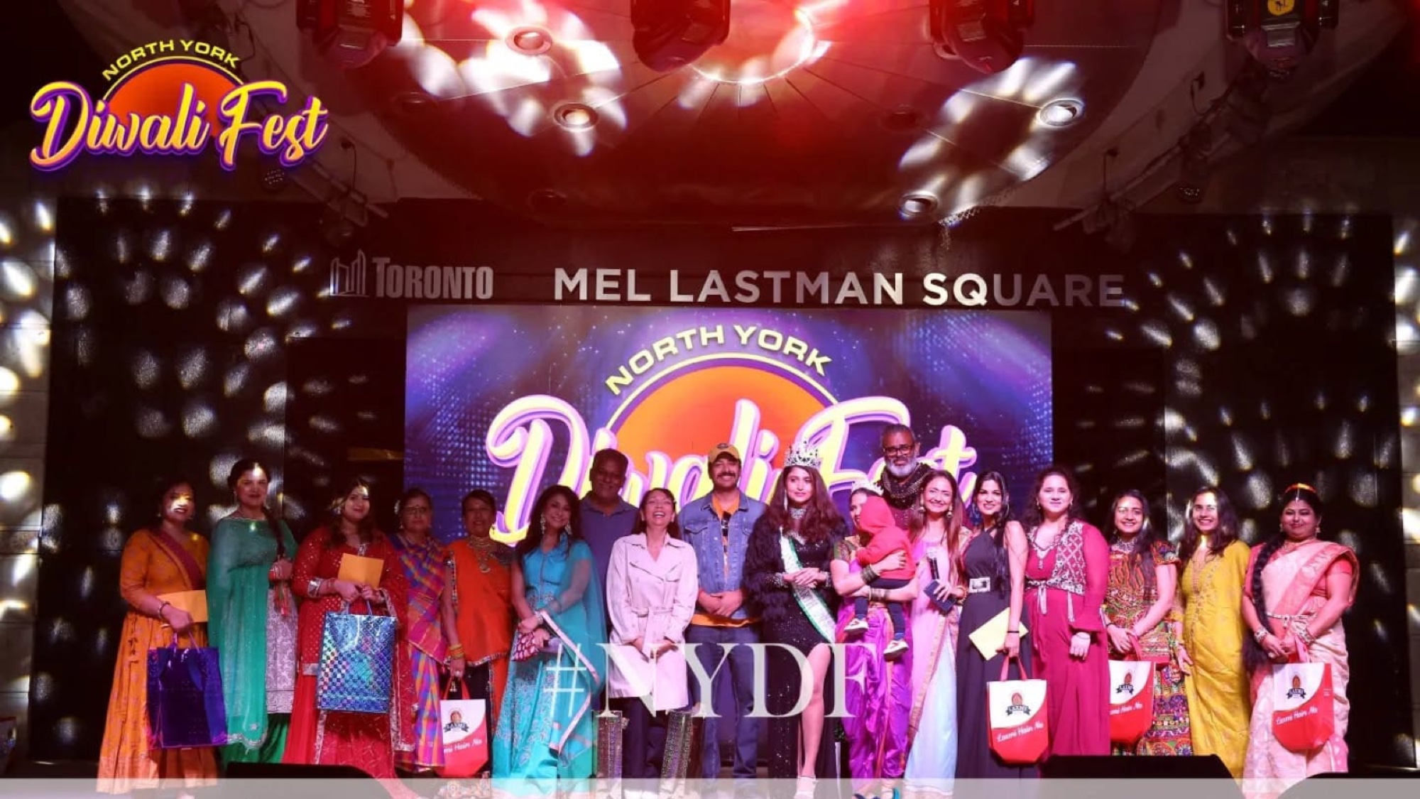 Stage group at North York Diwali Fest at Mel Lastman Square with festival branding on the screen behind them.