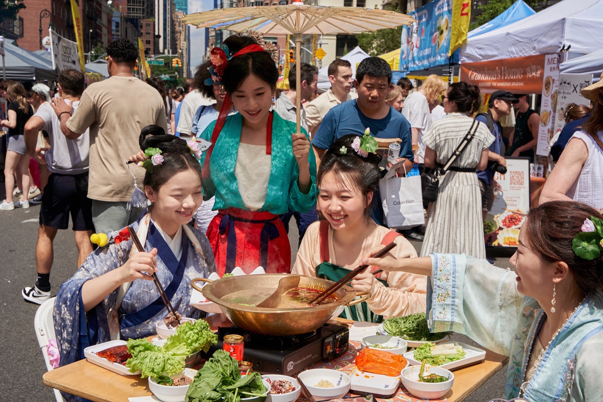 Guests in traditional dress sharing hot pot at outdoor vendor tents during a Panda Fest Asian food festival.