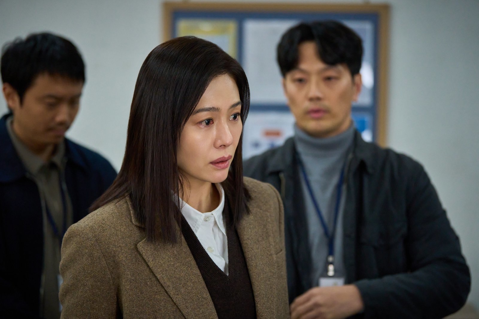 Kim Hyun-joo as the mother in Paradise Lost, tearful in a brown coat, with two men standing behind her in an office.