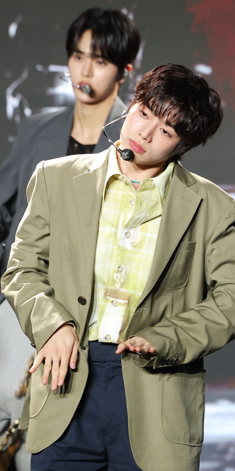 TEMPEST’s Hanbin onstage in an olive blazer and yellow plaid shirt during the As I Am showcase, headset mic on, mid-choreography.