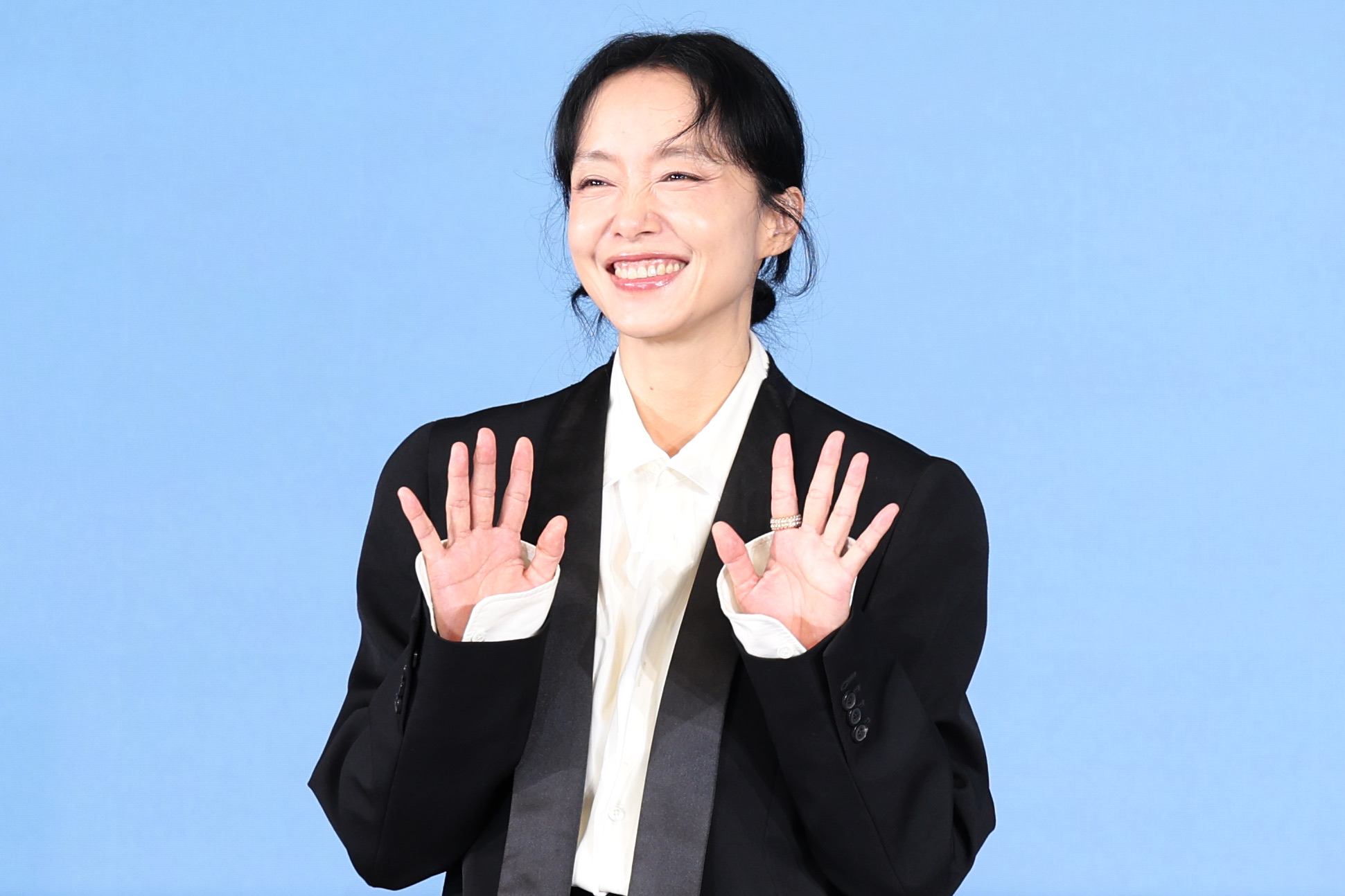 Jeon Do-yeon smiles with both hands raised, in a black blazer over a white shirt, at the Possible Love press conference in Seoul.