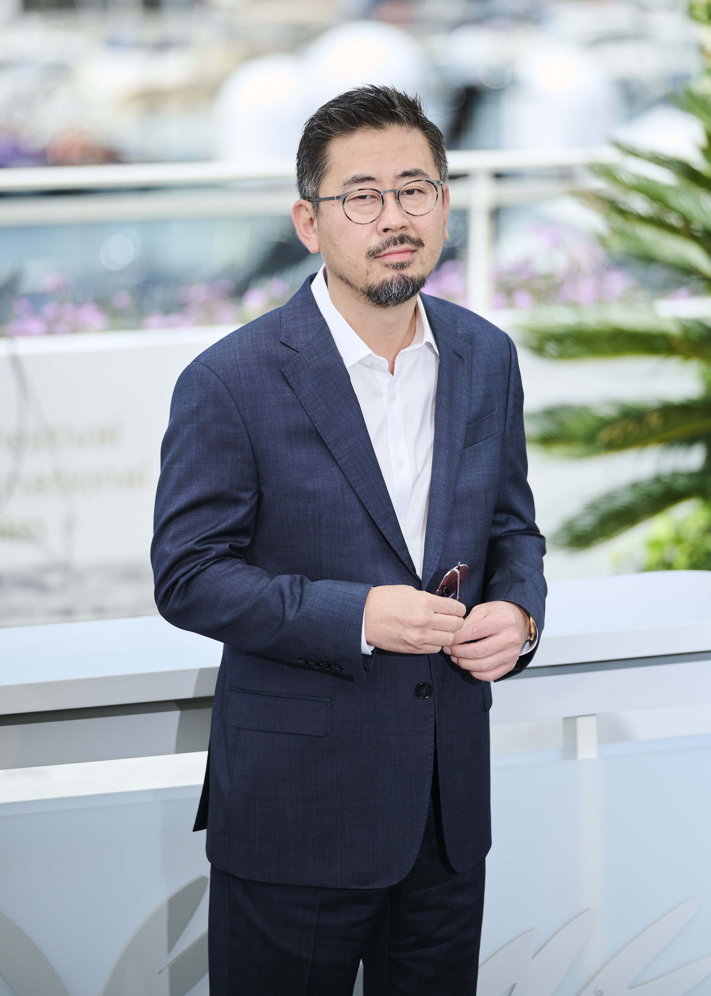 Director Na Hong-jin in a navy suit and glasses at the 2026 Cannes Film Festival photocall for Hope.