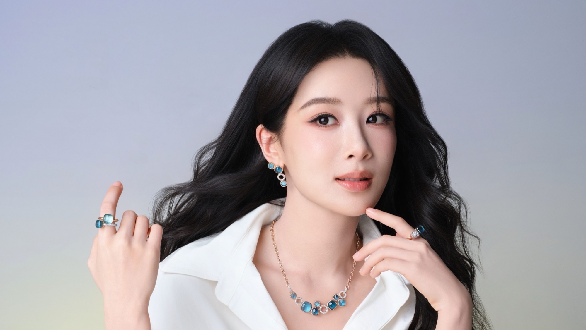Yang Zi in a white shirt wearing Pomellato Nudo blue topaz and rose-gold jewelry, including stacked rings, drop earrings, and a multi-pendant necklace.