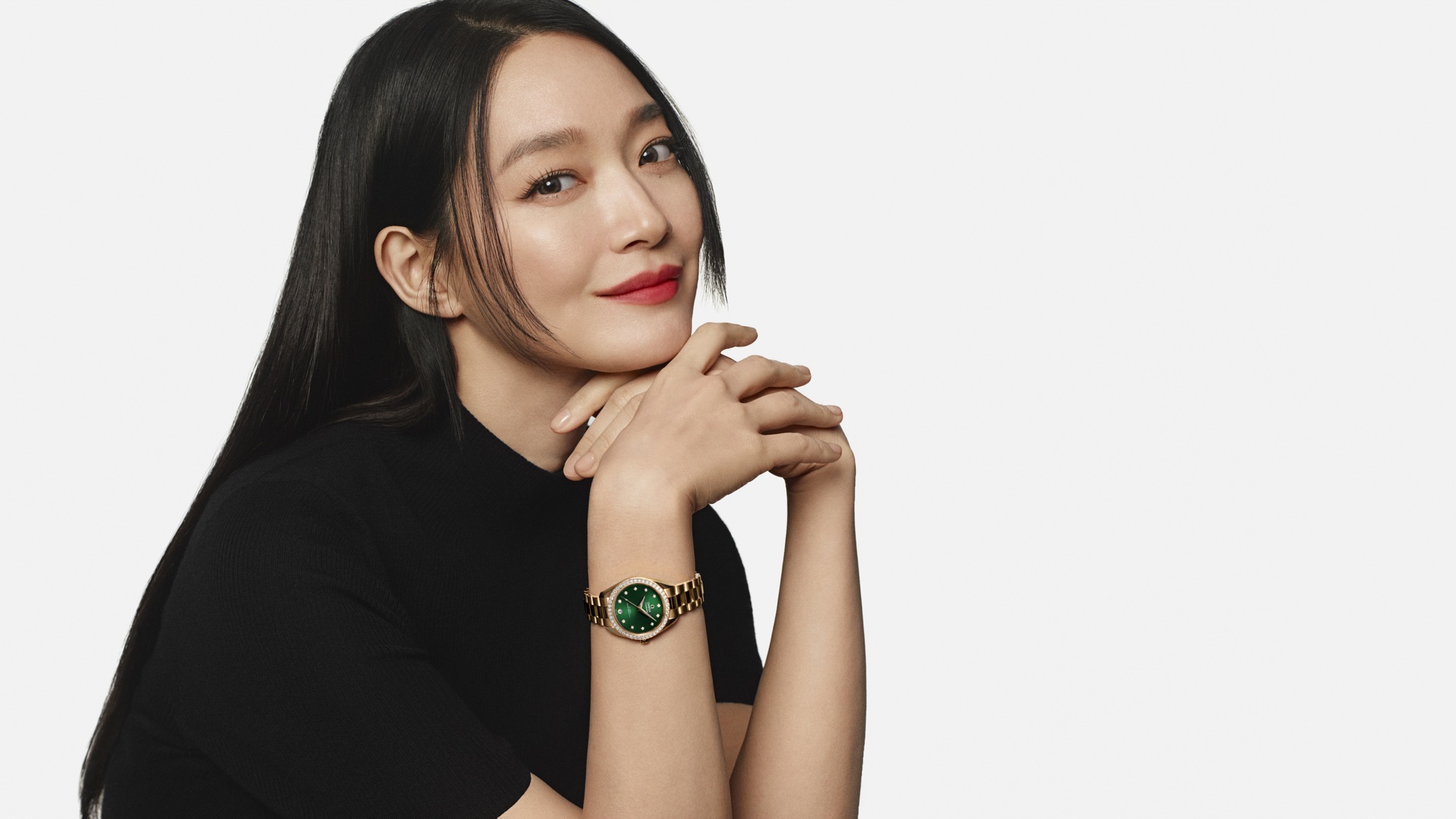 Shin Min-a resting her chin on her hands while wearing an Omega Aqua Terra 30 mm Moonshine Gold watch with a green dial and diamond bezel.