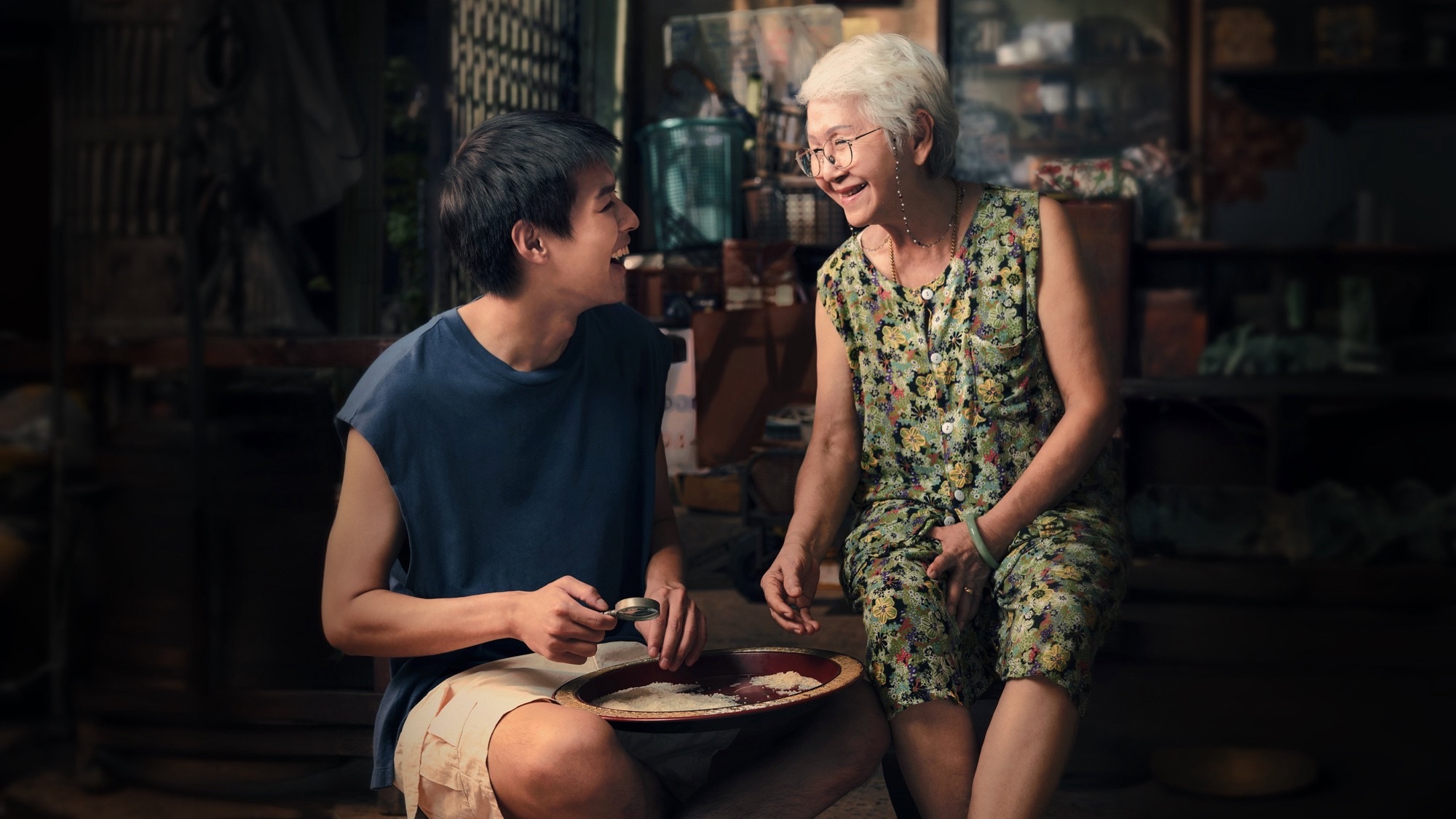 Putthipong Assaratanakul and Usha Seamkhum laugh together over a tray of rice in How to Make Millions Before Grandma Dies.