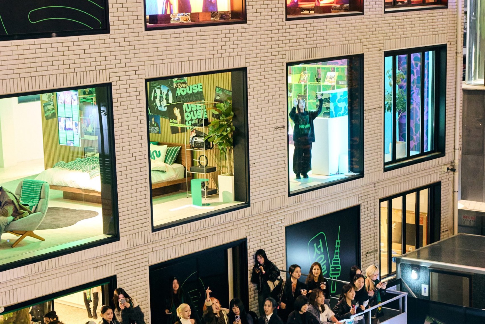 Exterior of a prior Spotify House Seoul activation at night, with branded window rooms, green HOUSE signage, and fans photographing the facade from a walkway.