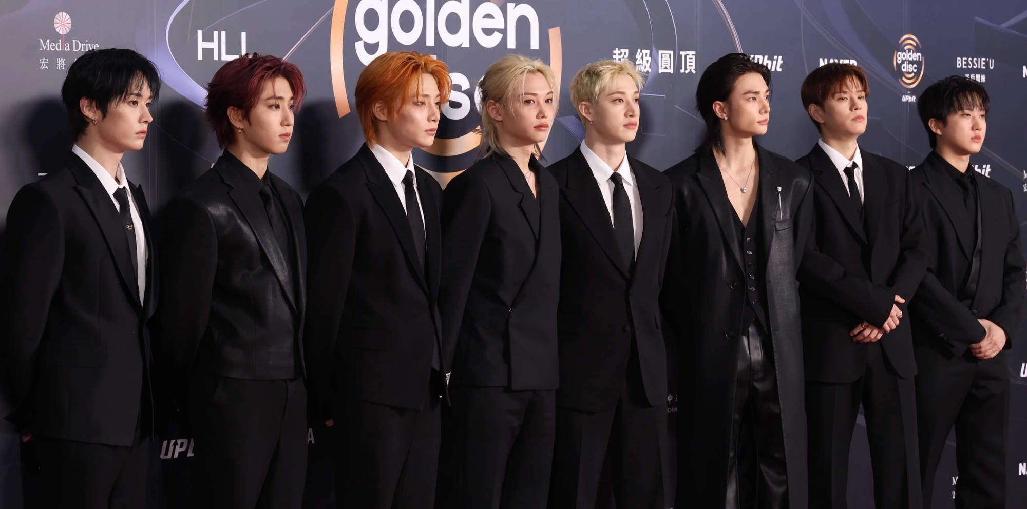 All eight Stray Kids members in black formalwear on the Golden Disc Awards red carpet against a dark awards-show backdrop.
