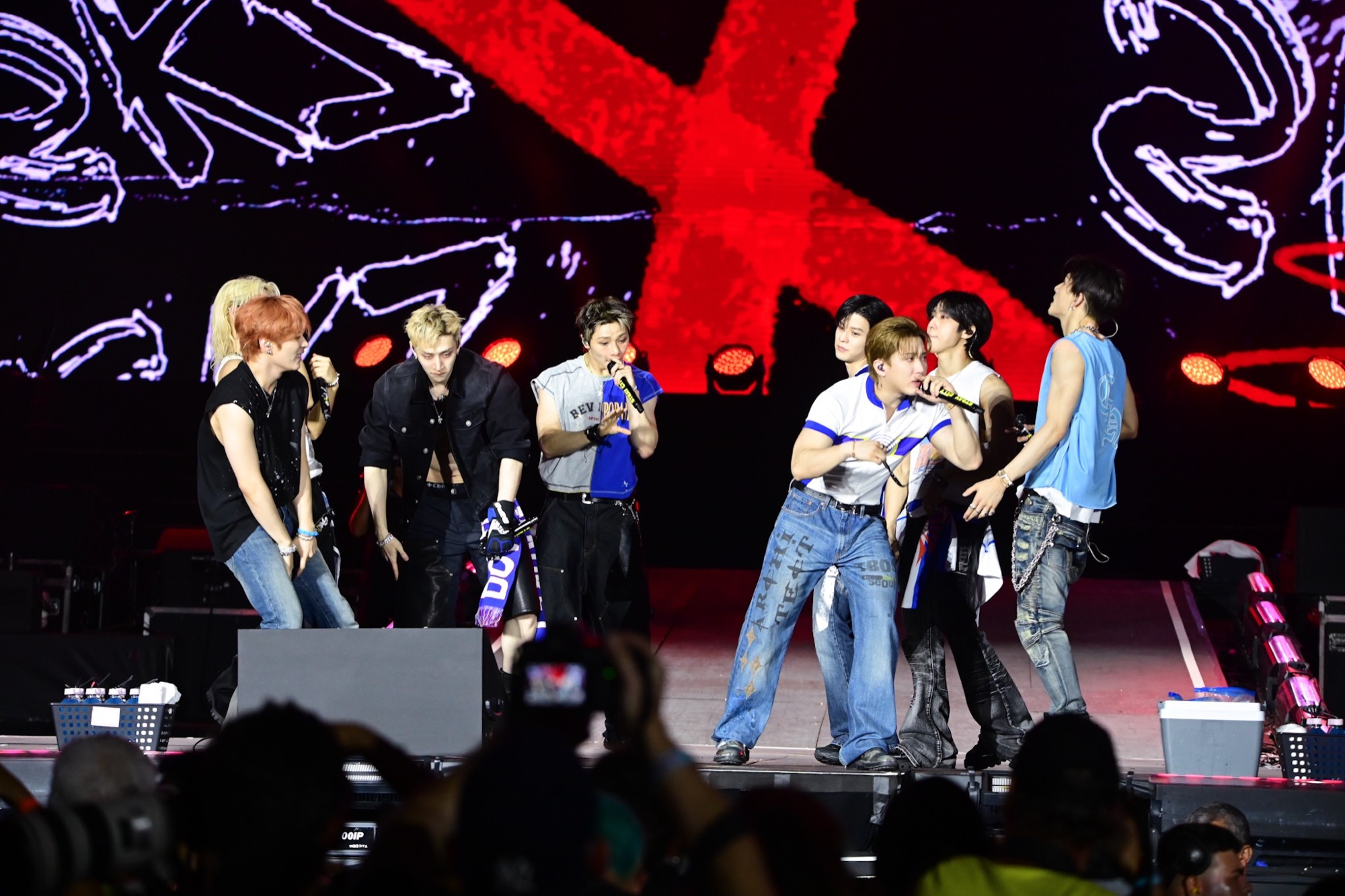 Stray Kids perform on Rock in Rio's Palco Mundo under red stage lights and an LED X backdrop, with the crowd visible in the foreground.