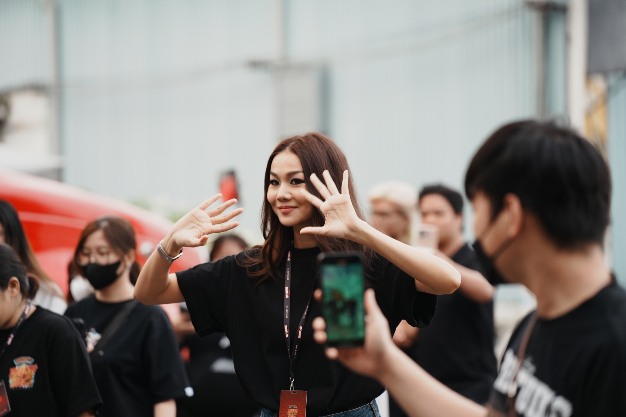 Thanh Hằng in a black crew shirt and lanyard greeting the camera on the production launch day for Mesdames Thanh Sắc in Ho Chi Minh City.