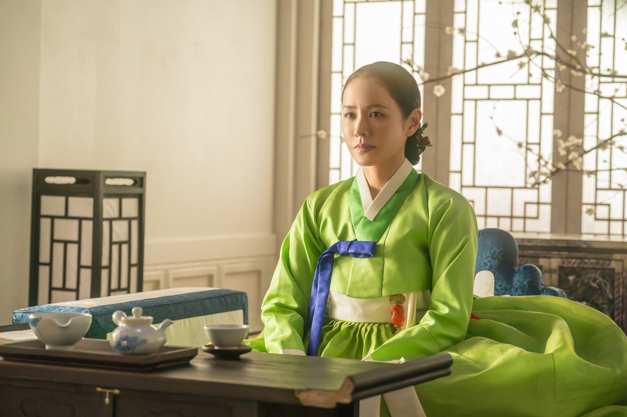 Son Ye-jin as Lady Cho sits in a lime-green hanbok at a tea table in Netflix's The Scandal.