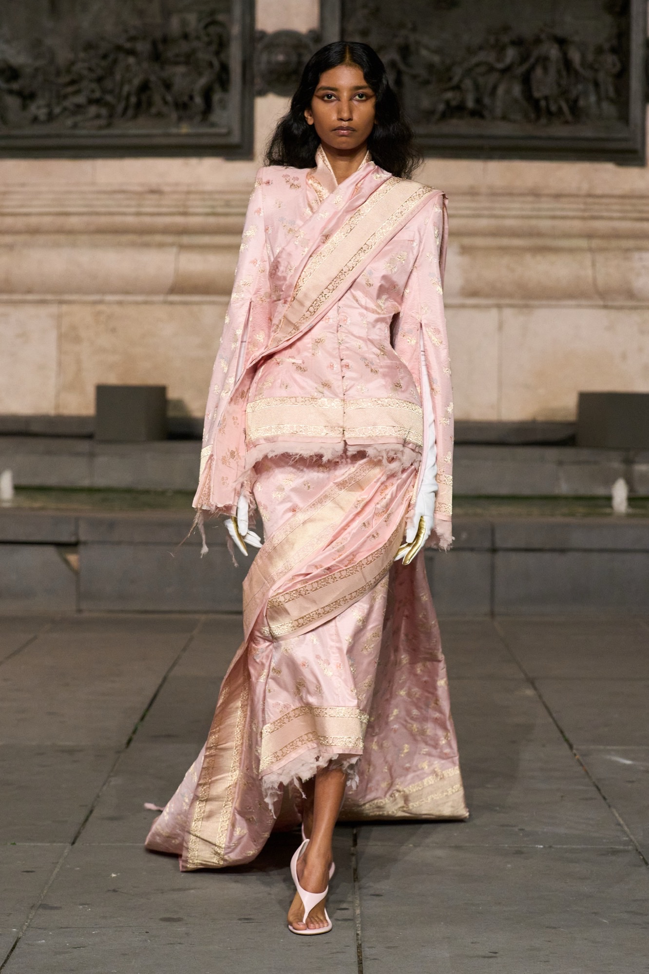 A model in a pale pink Tilfi Banaras saree-inspired jacket and drape walks the Matières Fécales runway at Place de la République.