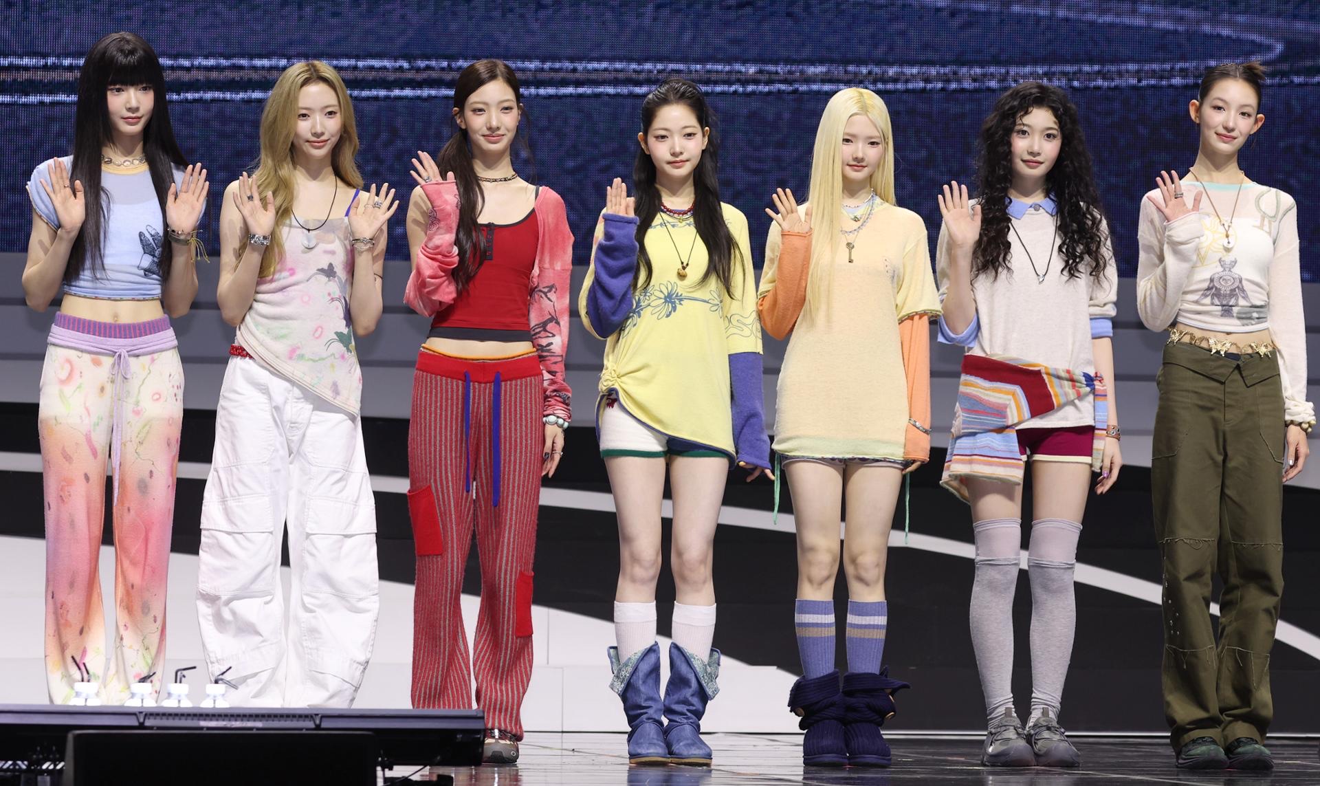 TUIDE's seven members stand in a line and wave onstage at their debut showcase for TUNE & PLAY.