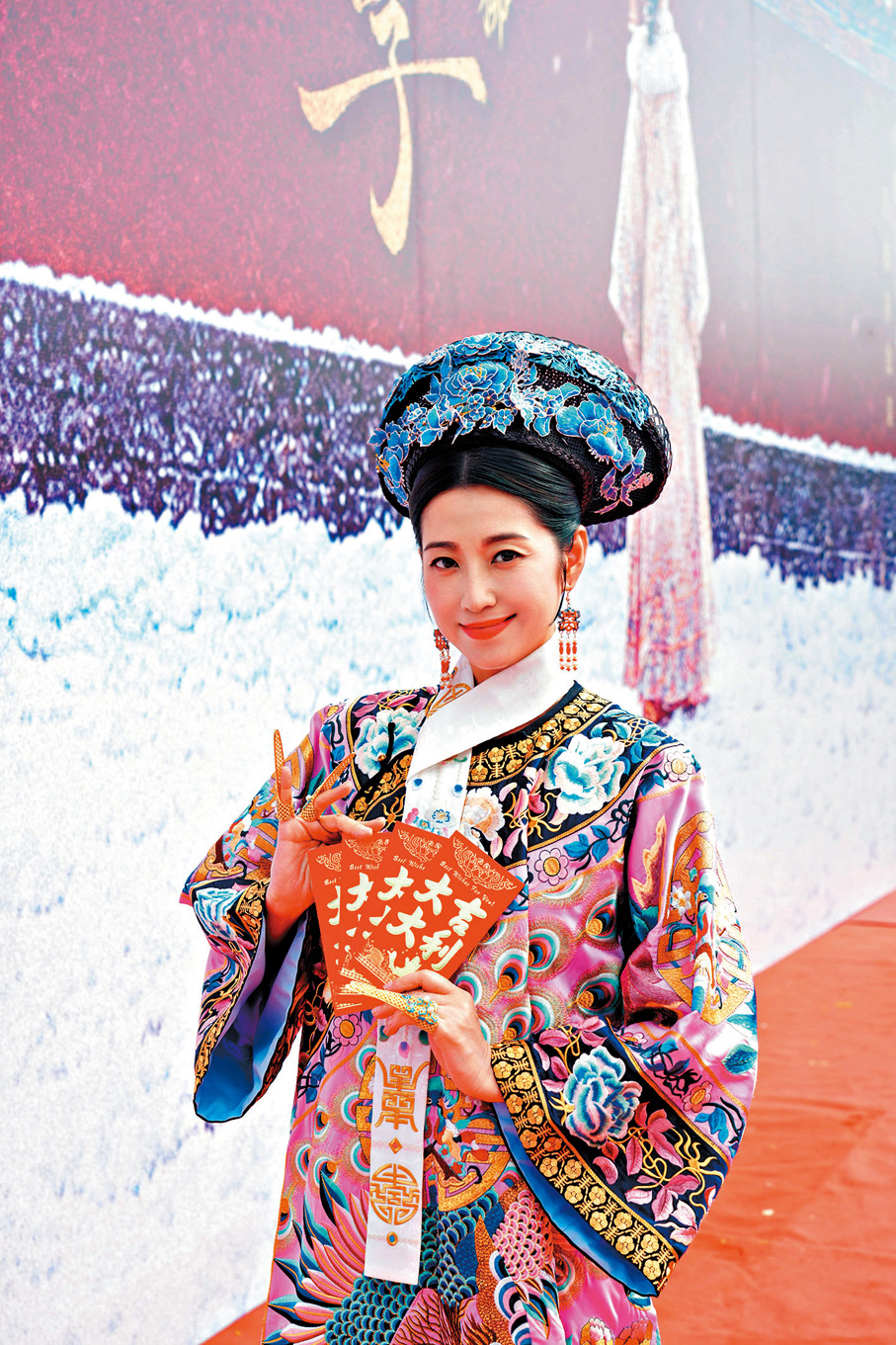Yoyo Chen in an embroidered Qing empress robe and a blue floral headdress, holding a red card at the War and Beauty short-drama ceremony.