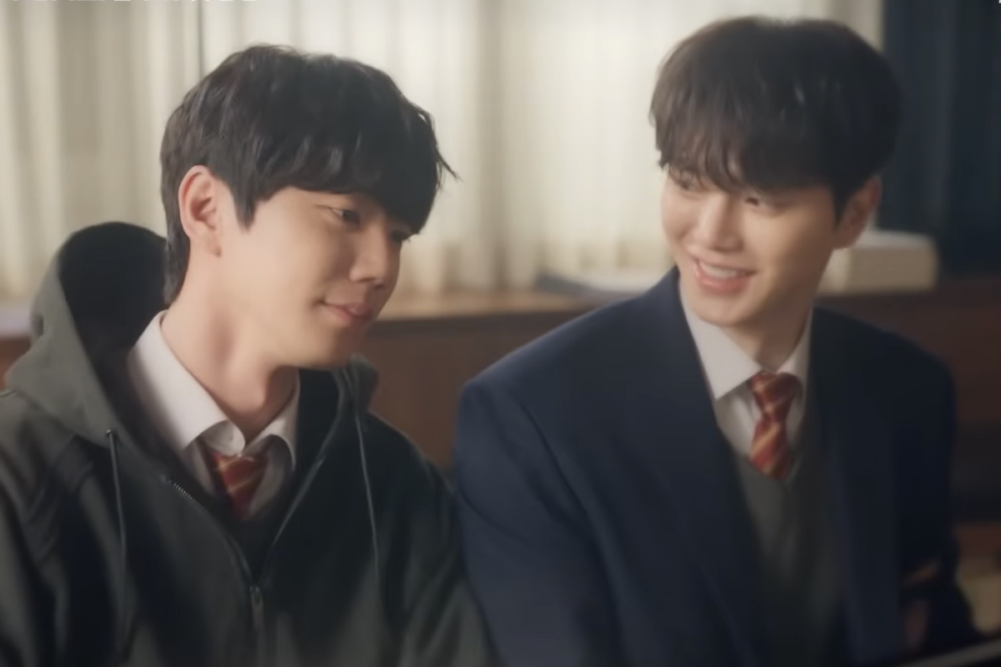 Song Kang and Lee Jun-young in school uniforms smiling at each other in a classroom still from Four Hands, Two Sonatas.